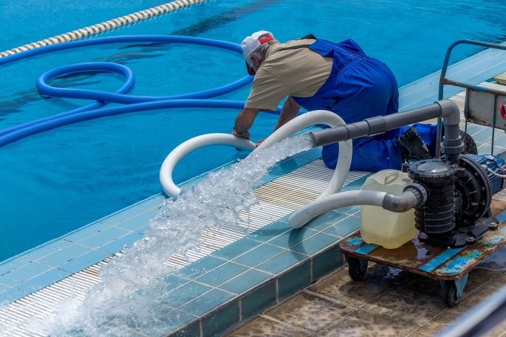 A Man Is Cleaning A Swimming Pool With A Hose — Col Davies Pools In Warners Bay, NSW