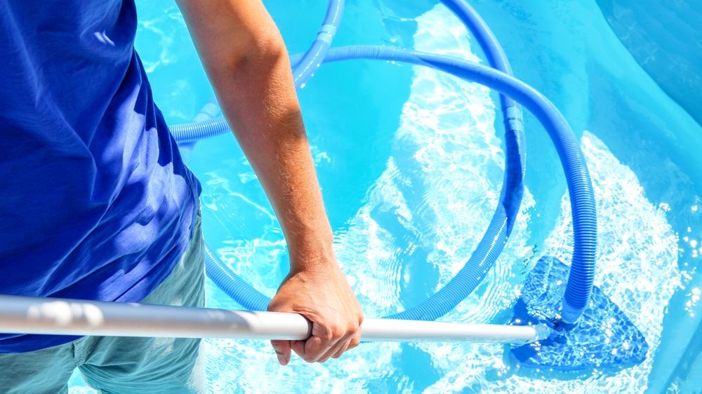 A Man Is Cleaning A Swimming Pool With A Vacuum — Col Davies Pools In Warners Bay, NSW