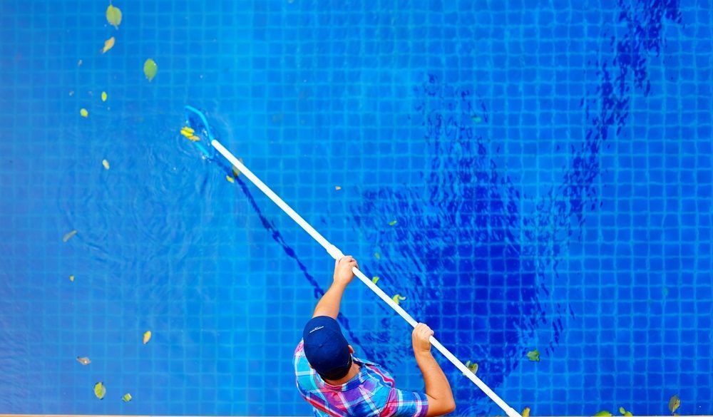 A Man Is Cleaning A Swimming Pool With A Leaf Rake — Col Davies Pools In Lake Macquarie, NSW