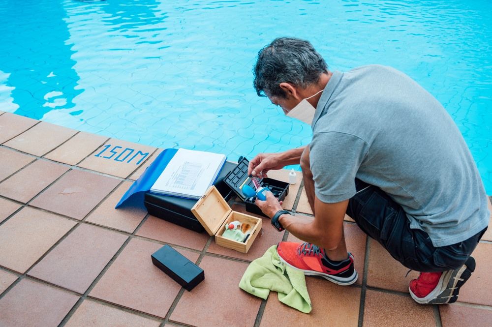 A Man Wearing A Mask Is Kneeling Next To A Swimming Pool — Col Davies Pools In Maitland, NSW
