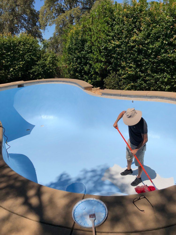 A Man Is Painting A Swimming Pool With A Roller — Col Davies Pools In Warners Bay, NSW