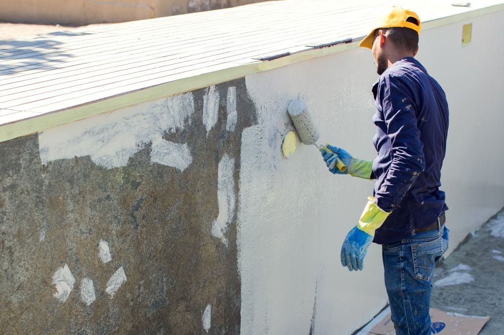 A Man Is Painting A Wall With A Roller — Col Davies Pools In Warners Bay, NSW