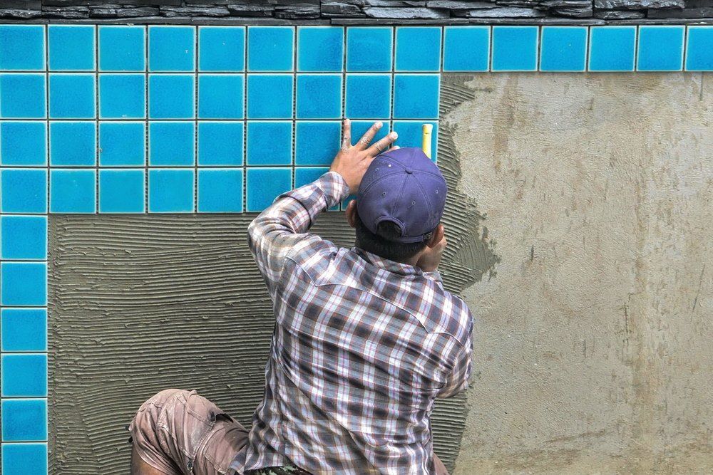 A Man Is Installing Blue Tiles On A Wall — Col Davies Pools In Maitland, NSW