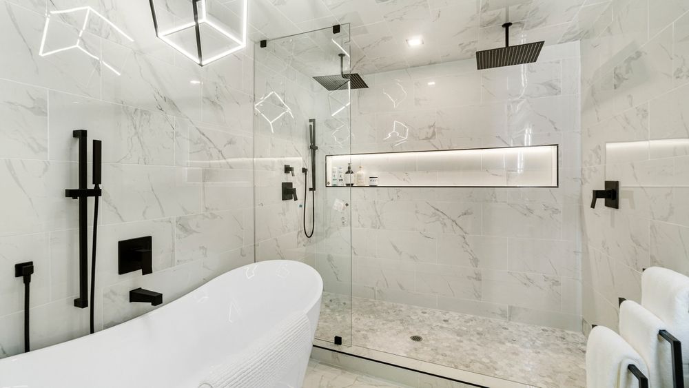 Modern white marble bathroom with glass shower, freestanding tub, and black fixtures