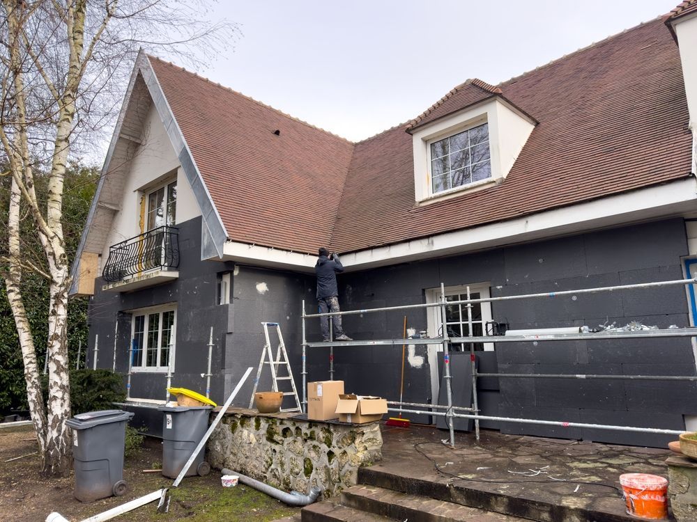 House exterior under renovation with scaffolding, ladder, and tools beside dark gray walls and a red-tiled roof
