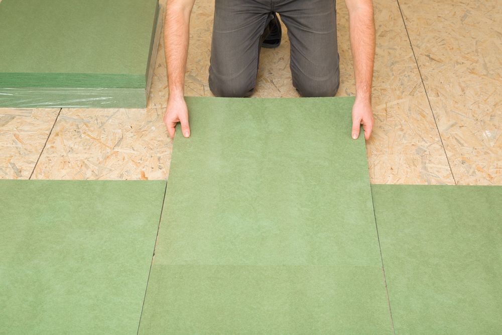 Person laying green floor tiles on a beige floor, aligning a central tile between existing tiles