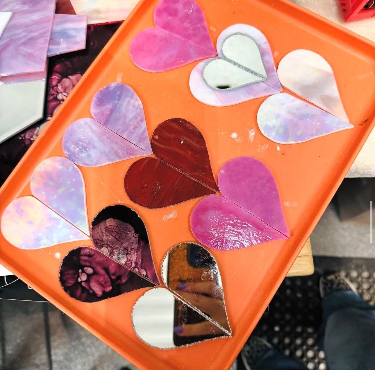 Person painting a colorful mosaic mandala on a wooden table with jars of paint nearby