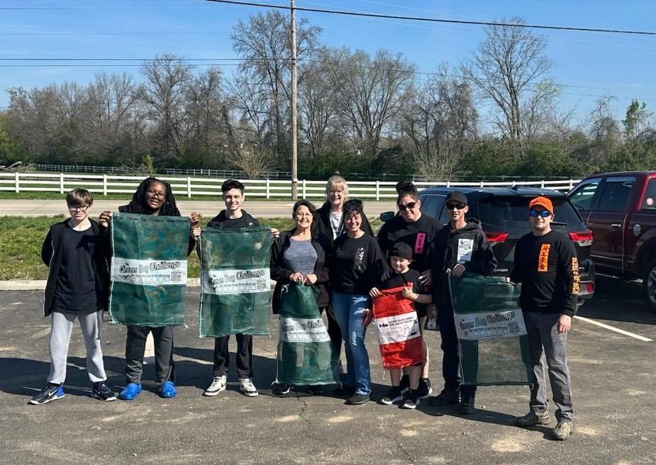 A group of people are standing in a parking lot holding volunteer trash cleanup bags.