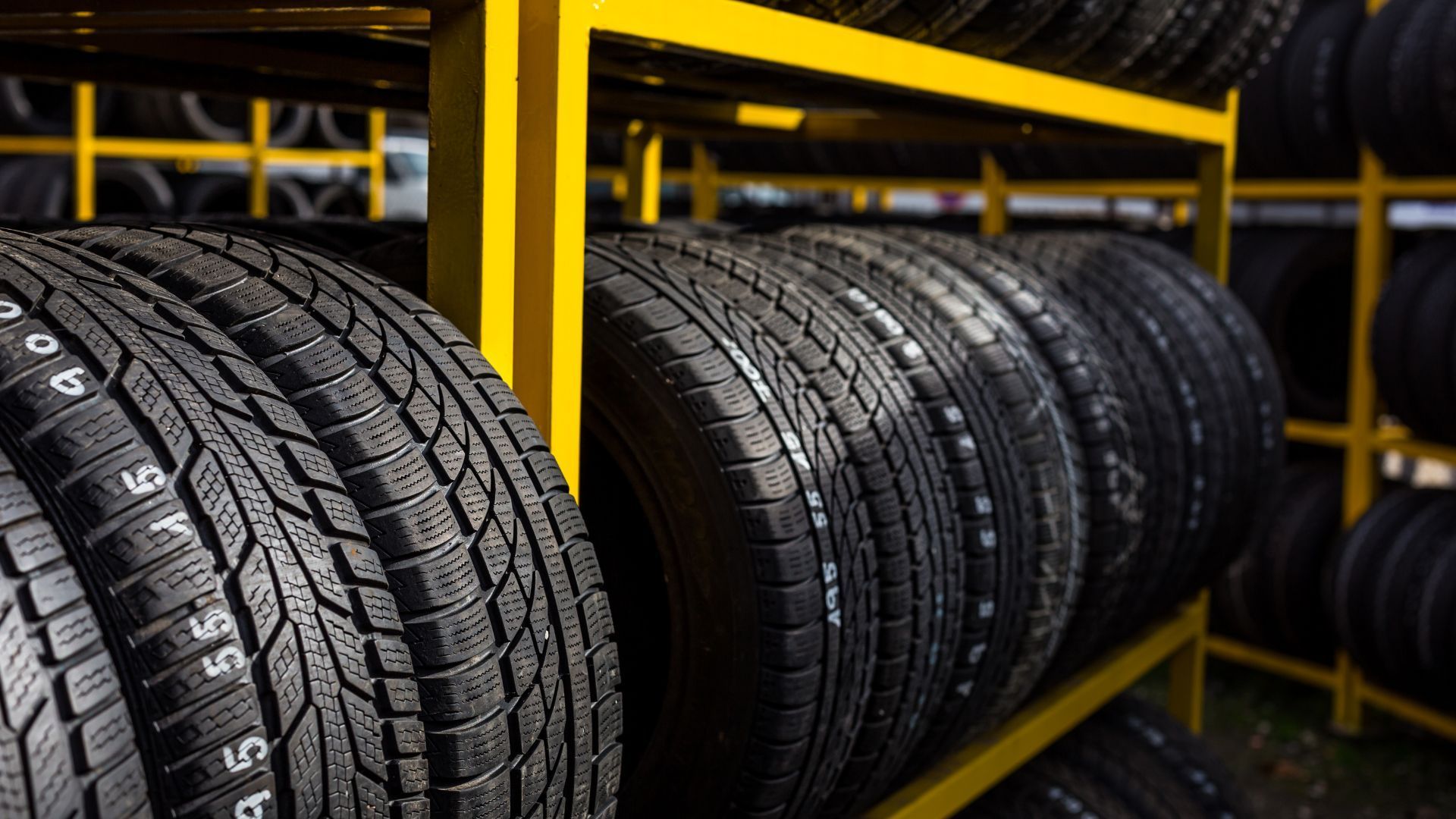 Stacked black tires on yellow metal racks in a warehouse storage area