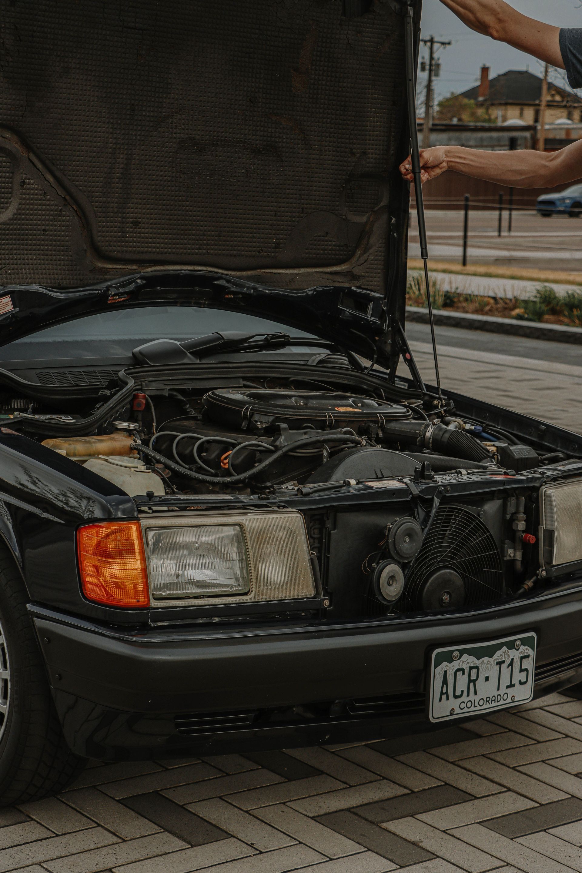 Black car with hood open, showing engine bay in a parking lot.