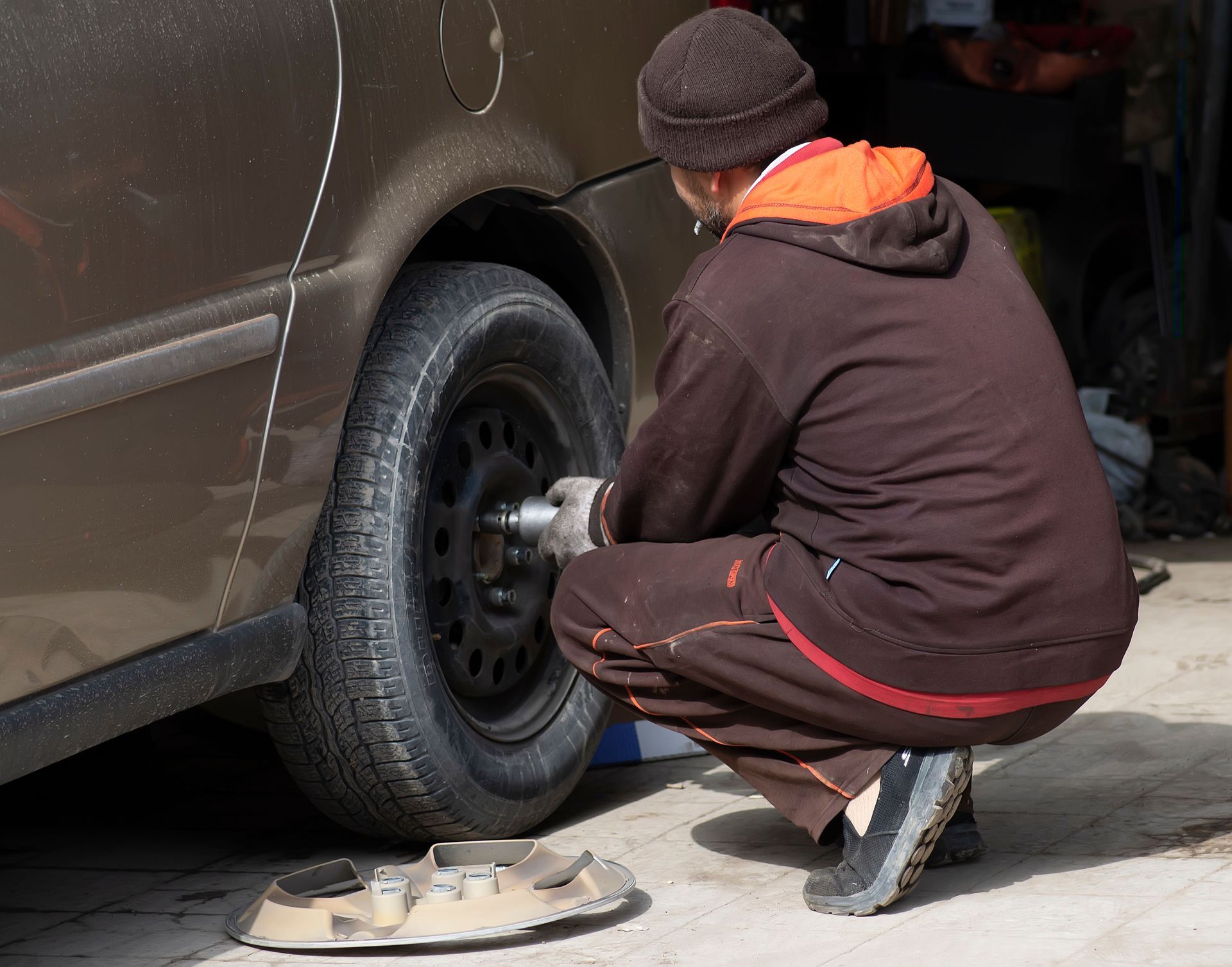 Person crouches by a van, changing a tire with a lug wrench.