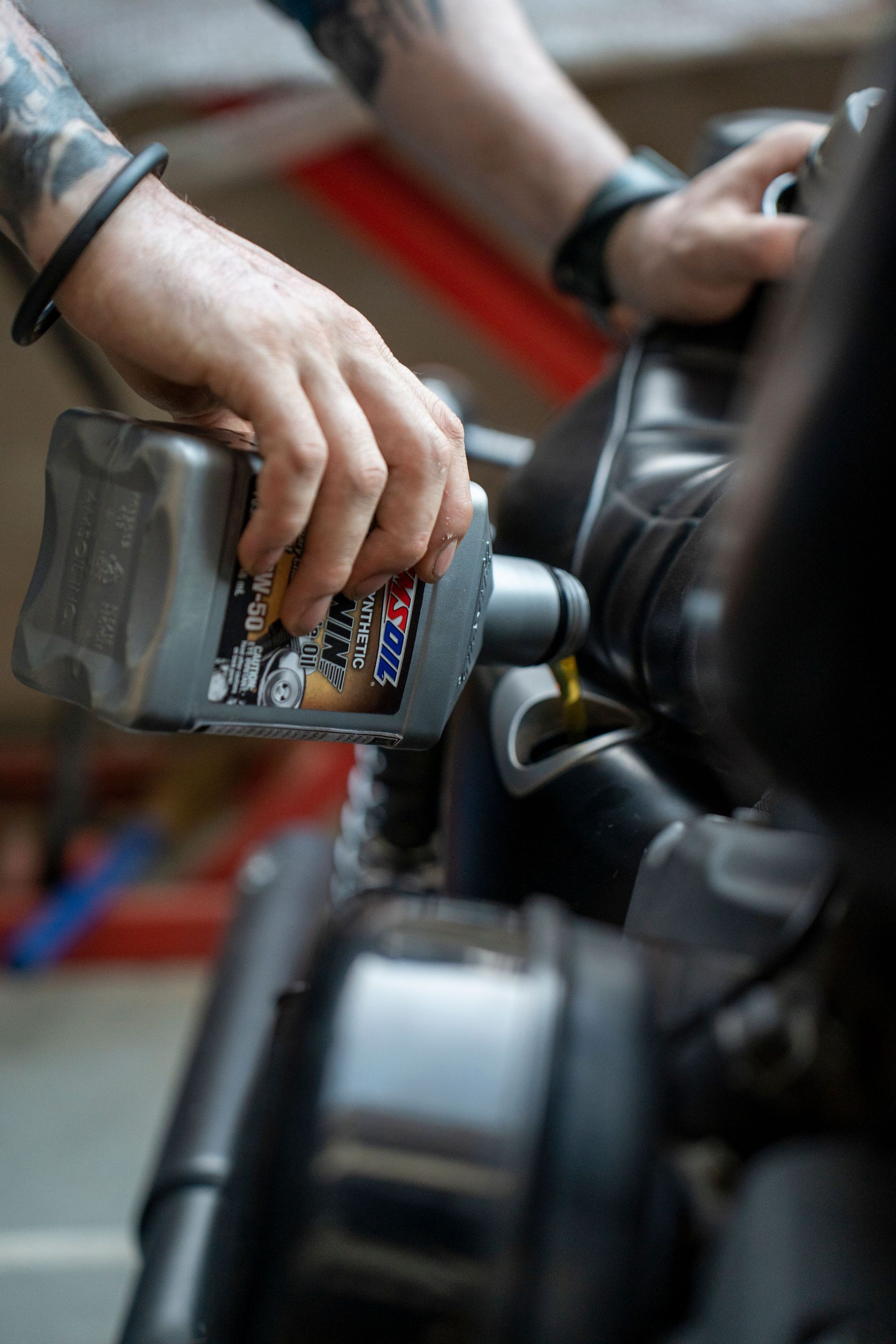 Hands pouring motor oil into a car engine in a workshop