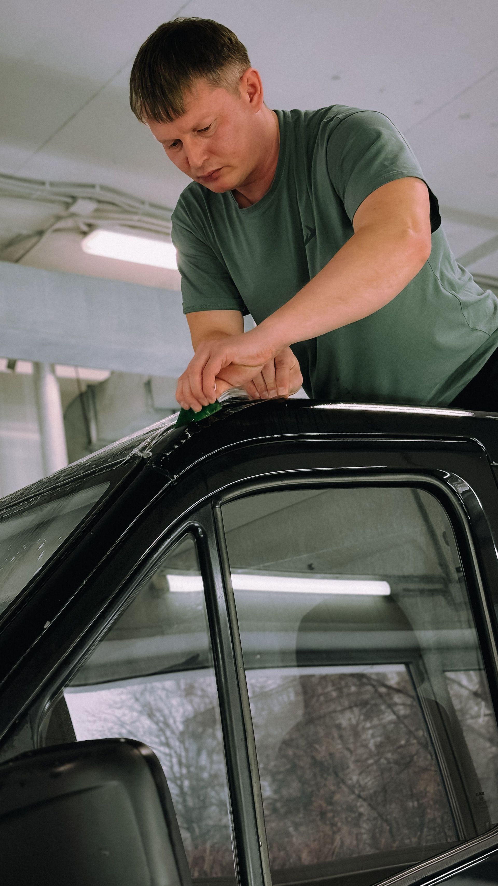 Mechanic kneeling beside a blue car, inspecting the wheel with a tire tool in a garage