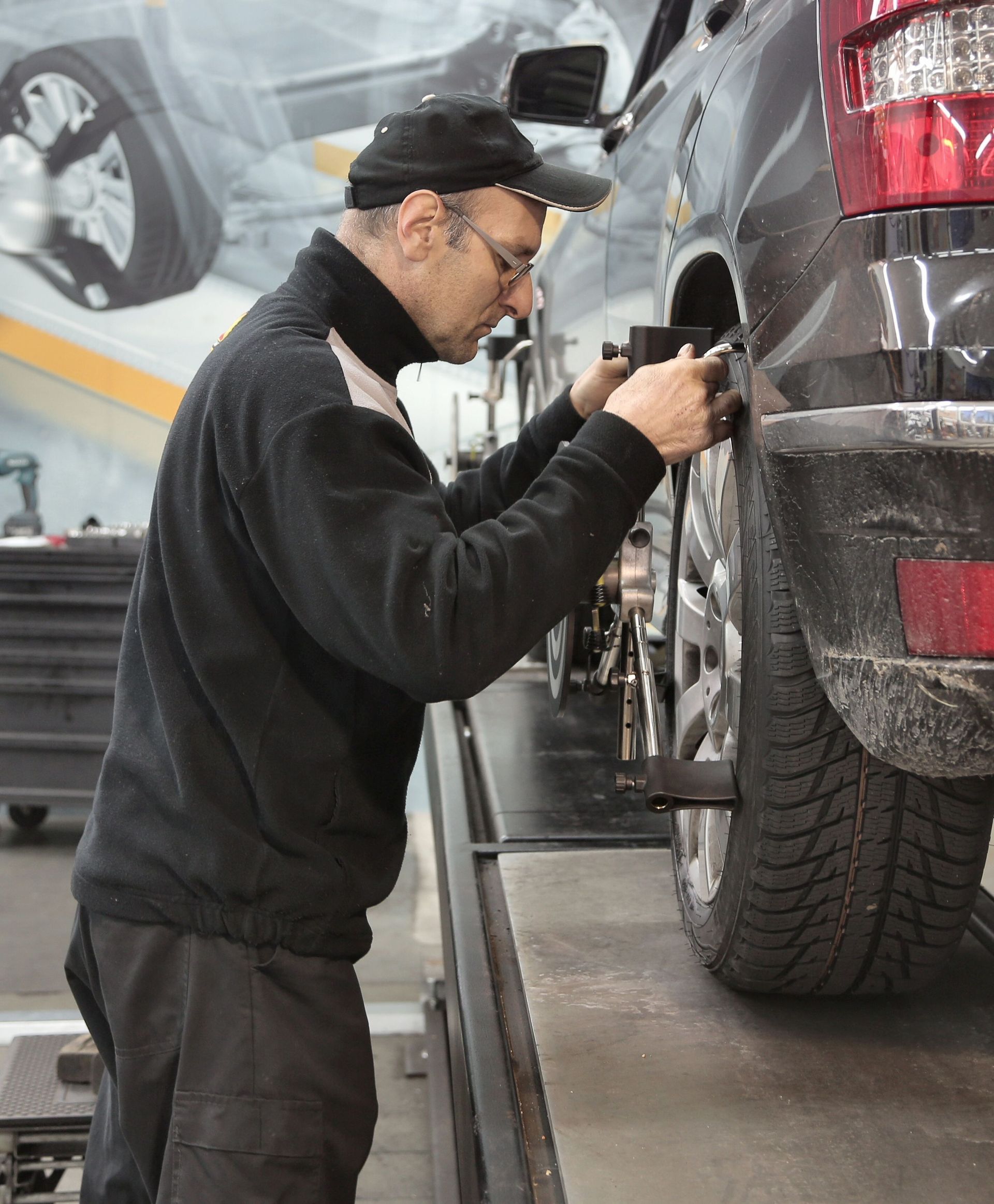 Mechanic inspecting the wheel of a black SUV on a lift in an auto repair shop