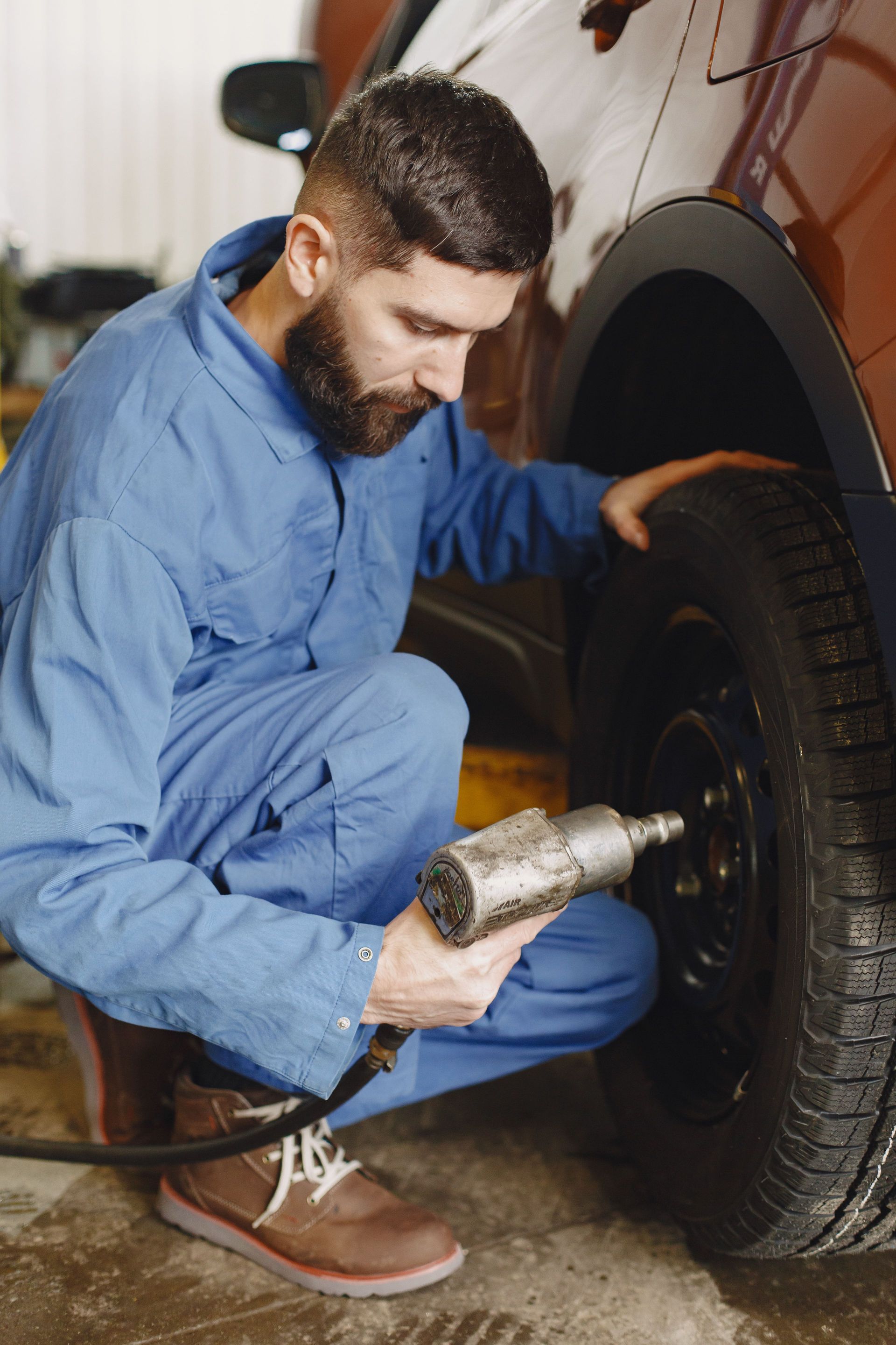 Mechanic in blue coveralls using a heat gun to inspect a car tire near the wheel well