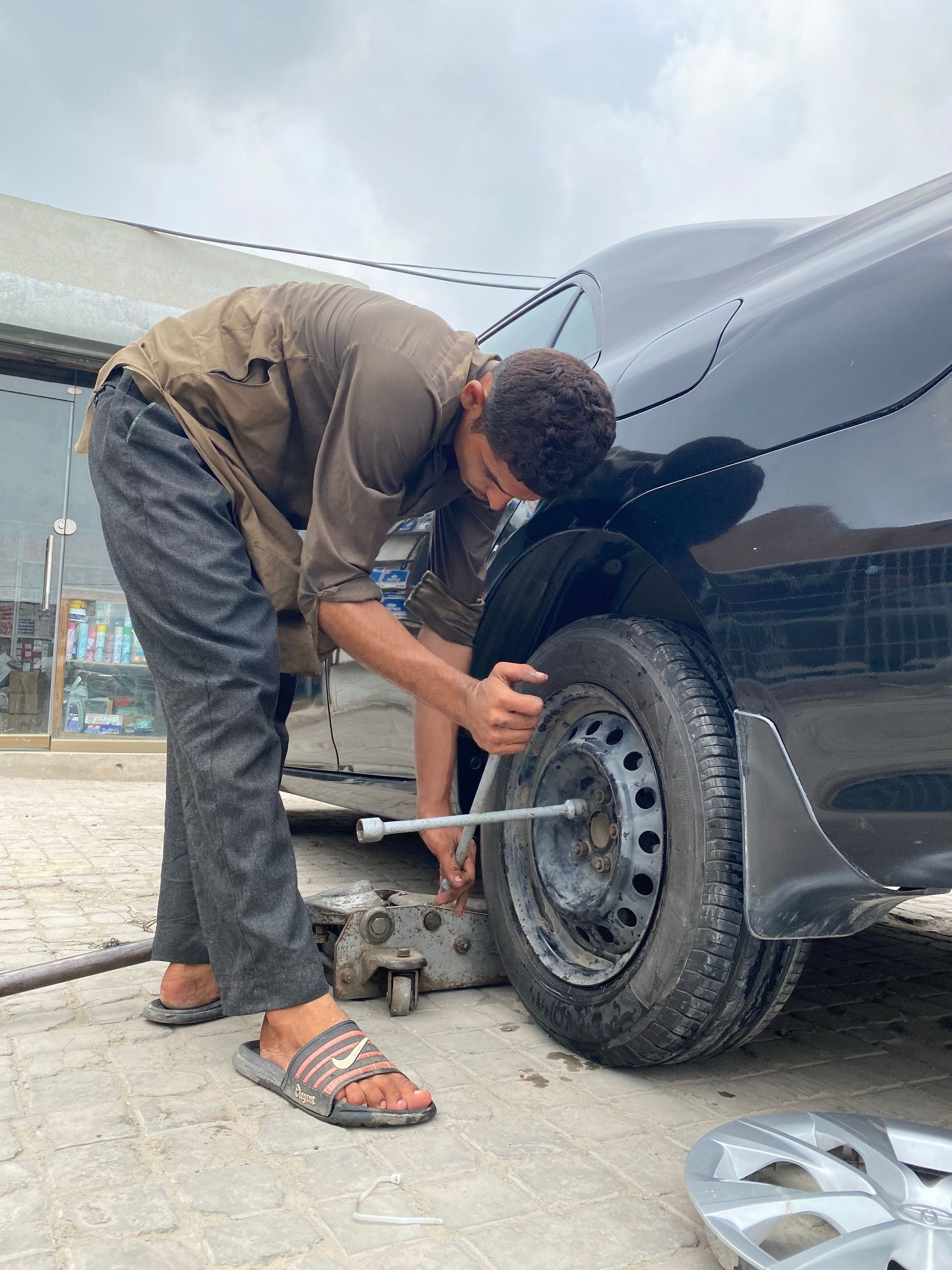 Mechanic crouches beside a dark car, tightening a wheel lug on the front tire.