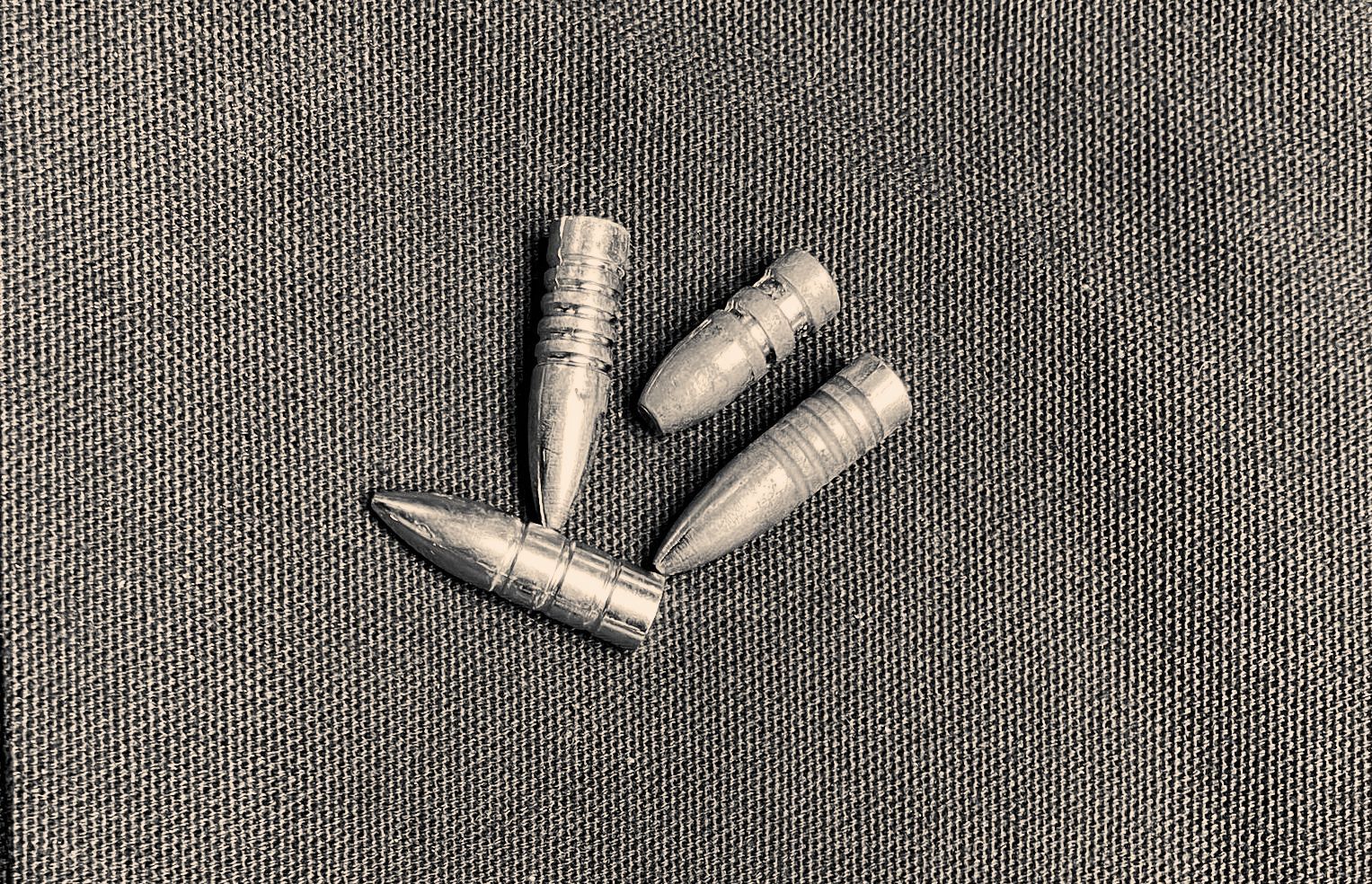 Three bullets are laying on a gray cloth.