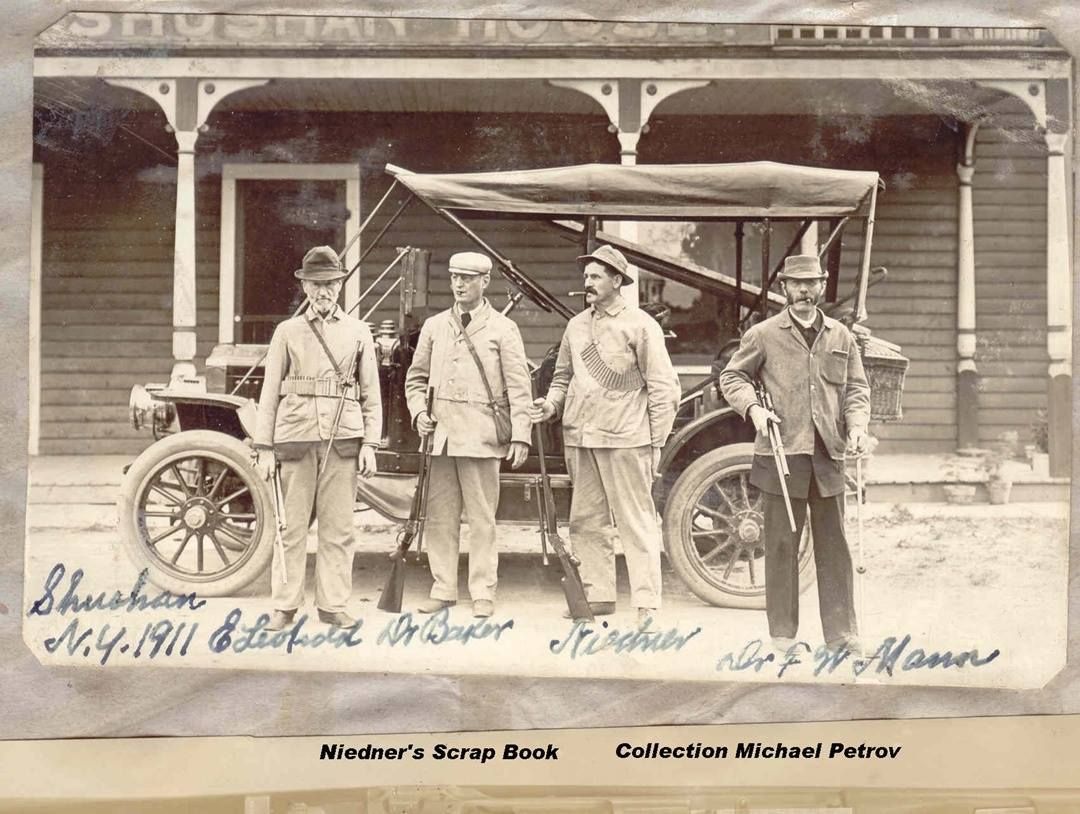 A black and white photo of four men standing in front of an old car
