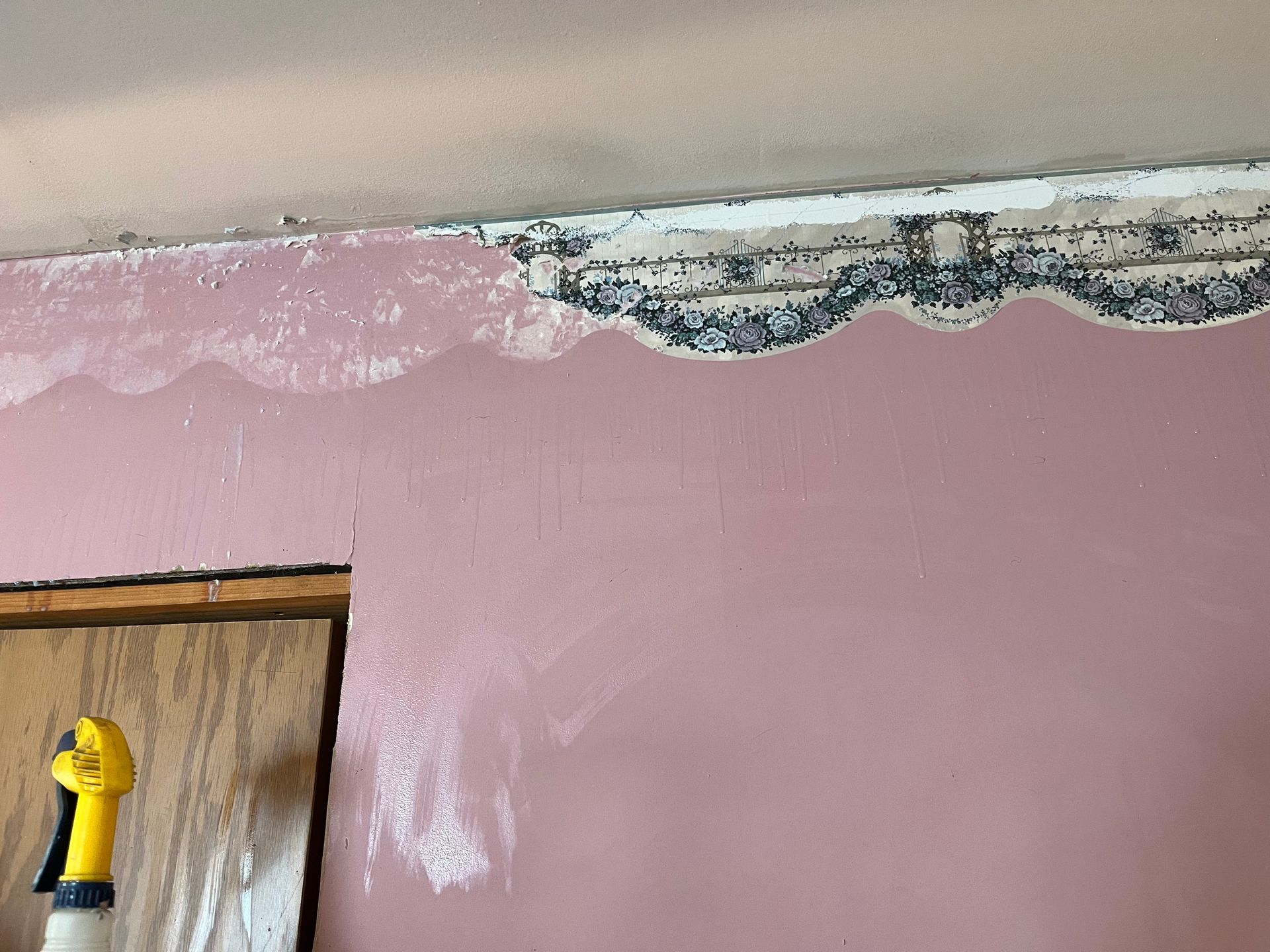 A wall partially painted dusty pink, revealing an old patterned wallpaper border underneath near the ceiling.