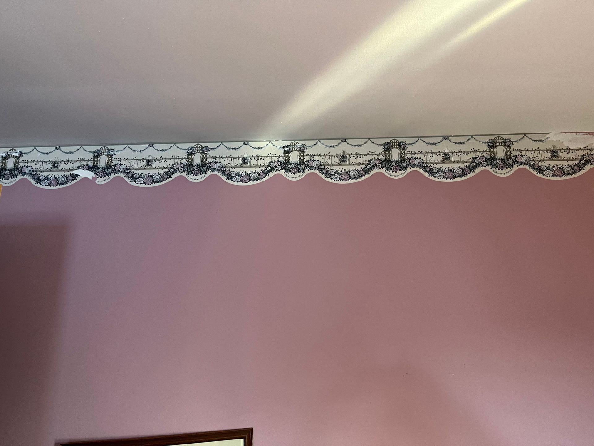 A pink wall featuring a decorative, scalloped black and white wallpaper border near the ceiling.