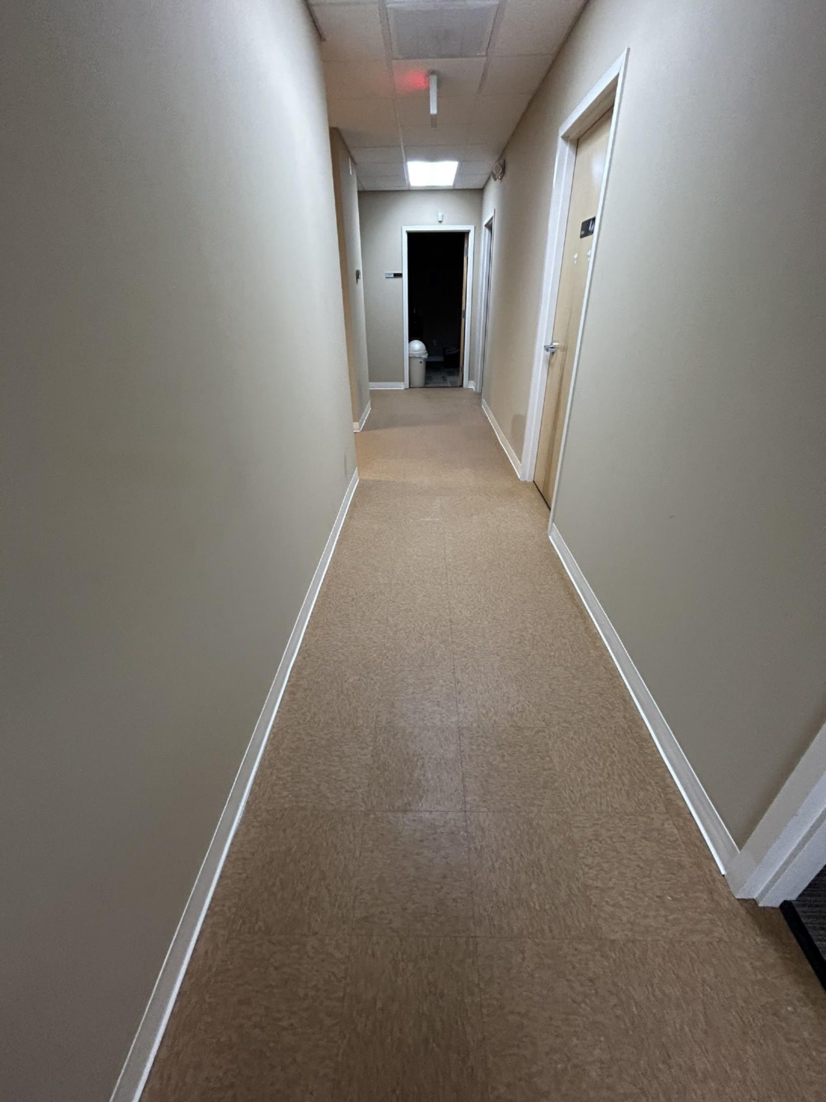 Narrow hallway with beige walls, tan carpet, and doors on the right side.
