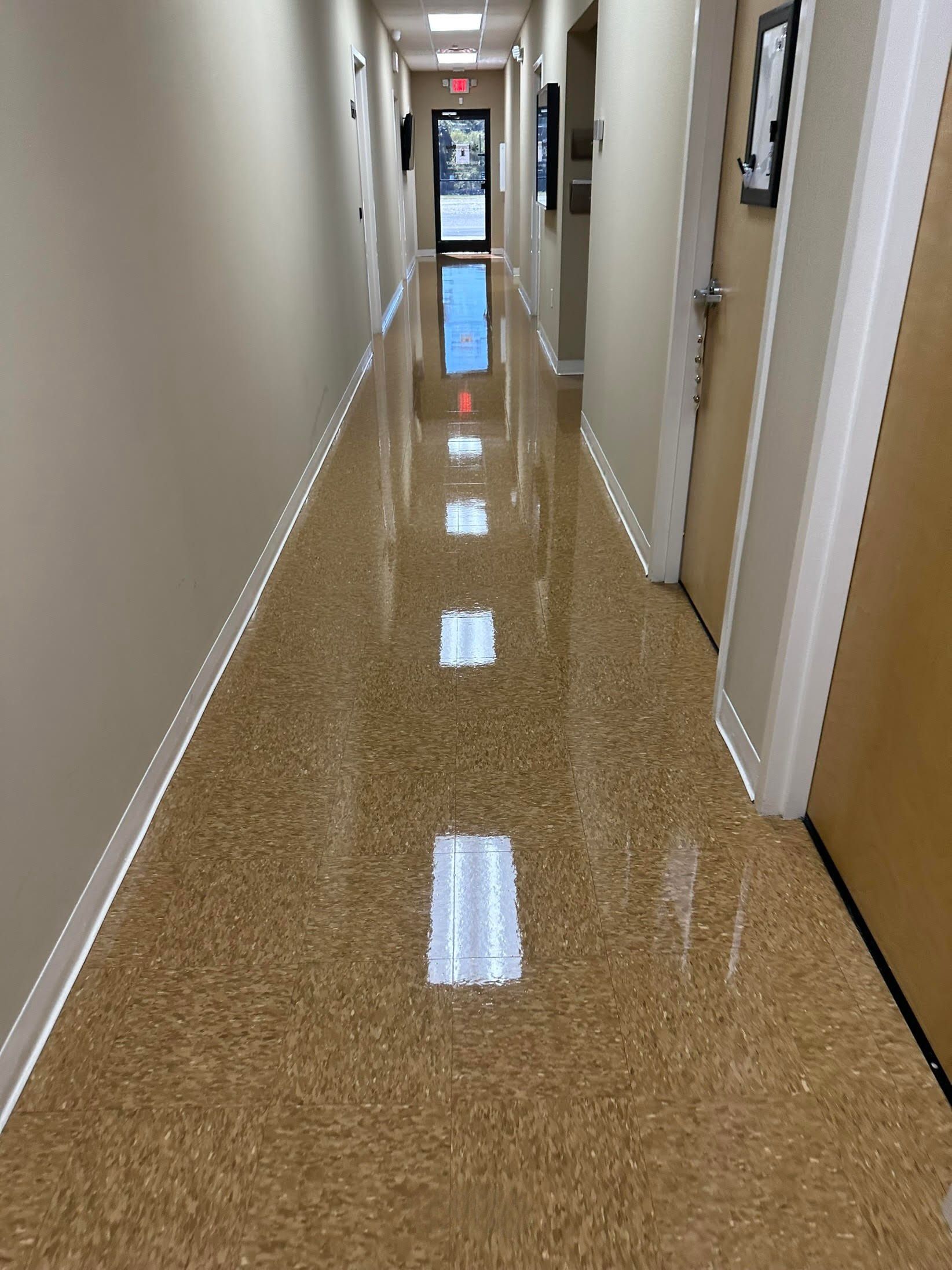 Long hallway with shiny, speckled flooring; beige walls, doors, and a distant doorway.