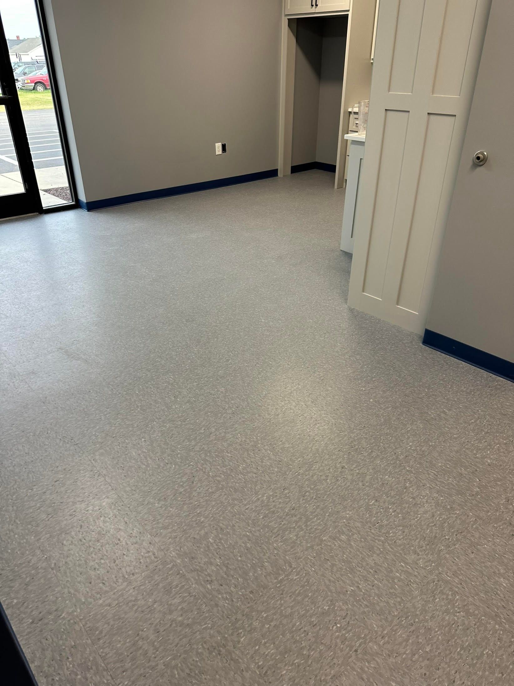 Grey speckled floor in an empty room with gray walls and a blue trim. A white cabinet is in the background.