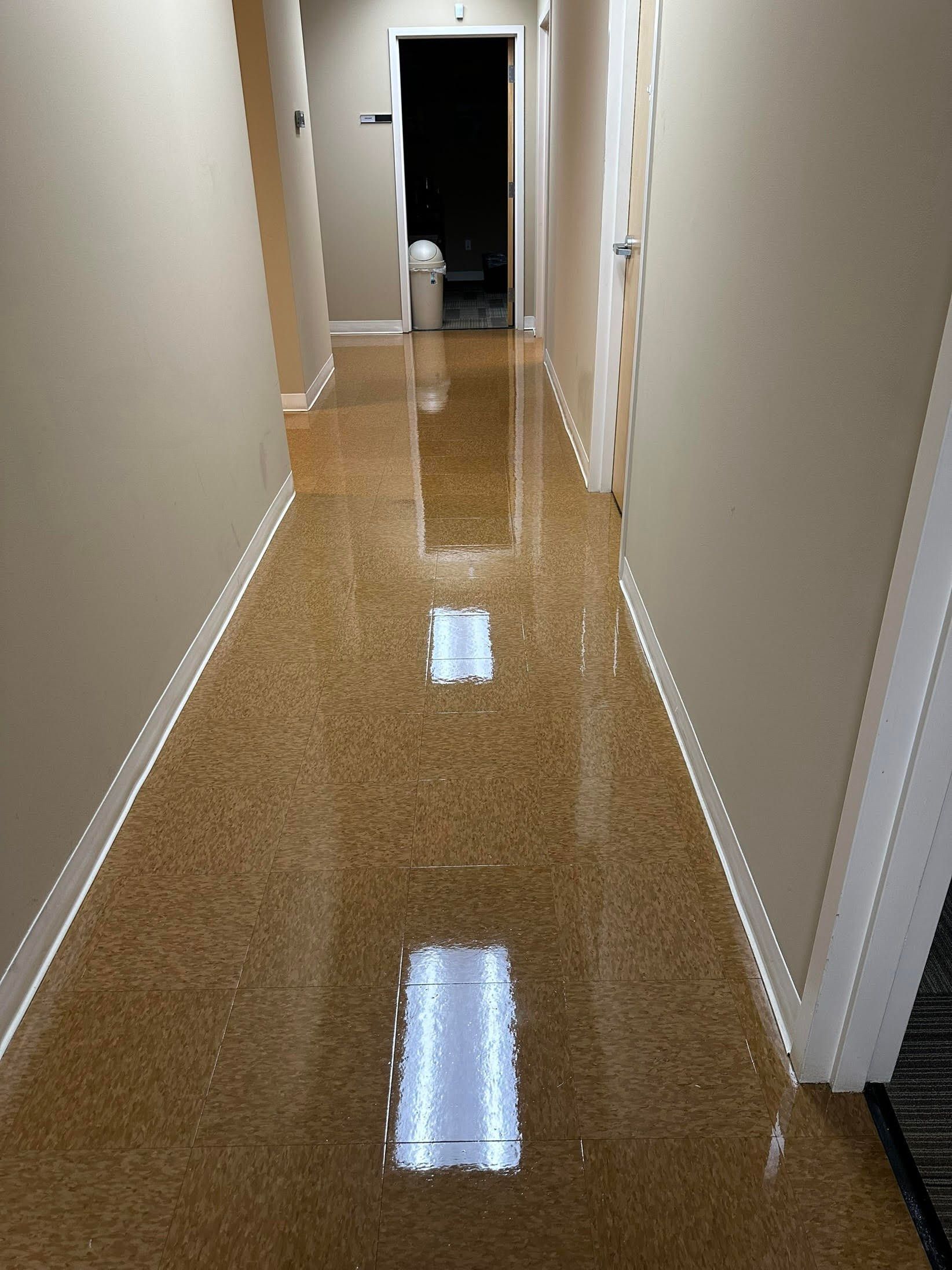 A narrow hallway with tan walls and a shiny speckled brown floor. A doorway is visible at the end.