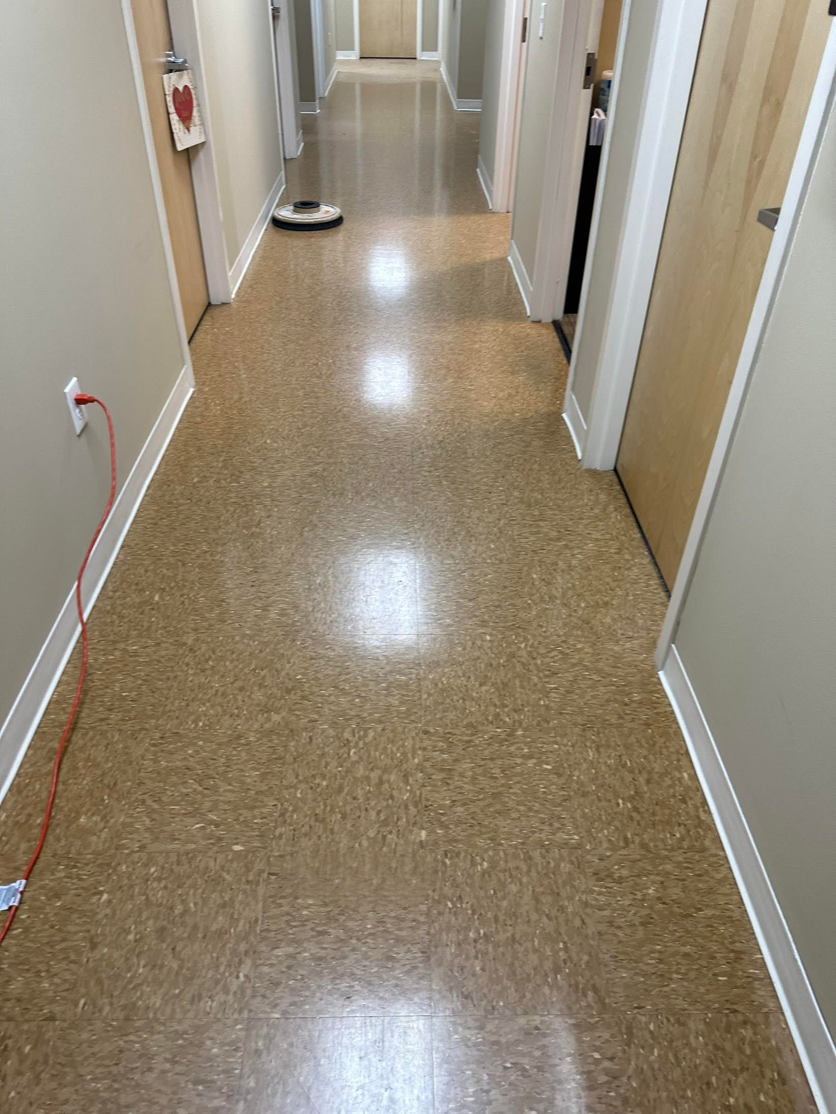 Long hallway with light brown speckled flooring, beige walls, and closed wooden doors.