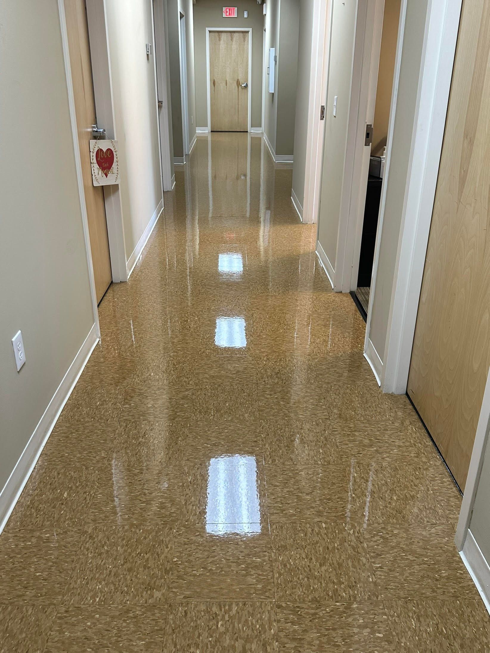 Hallway with shiny, speckled floor, doors on both sides, and overhead lights reflecting.