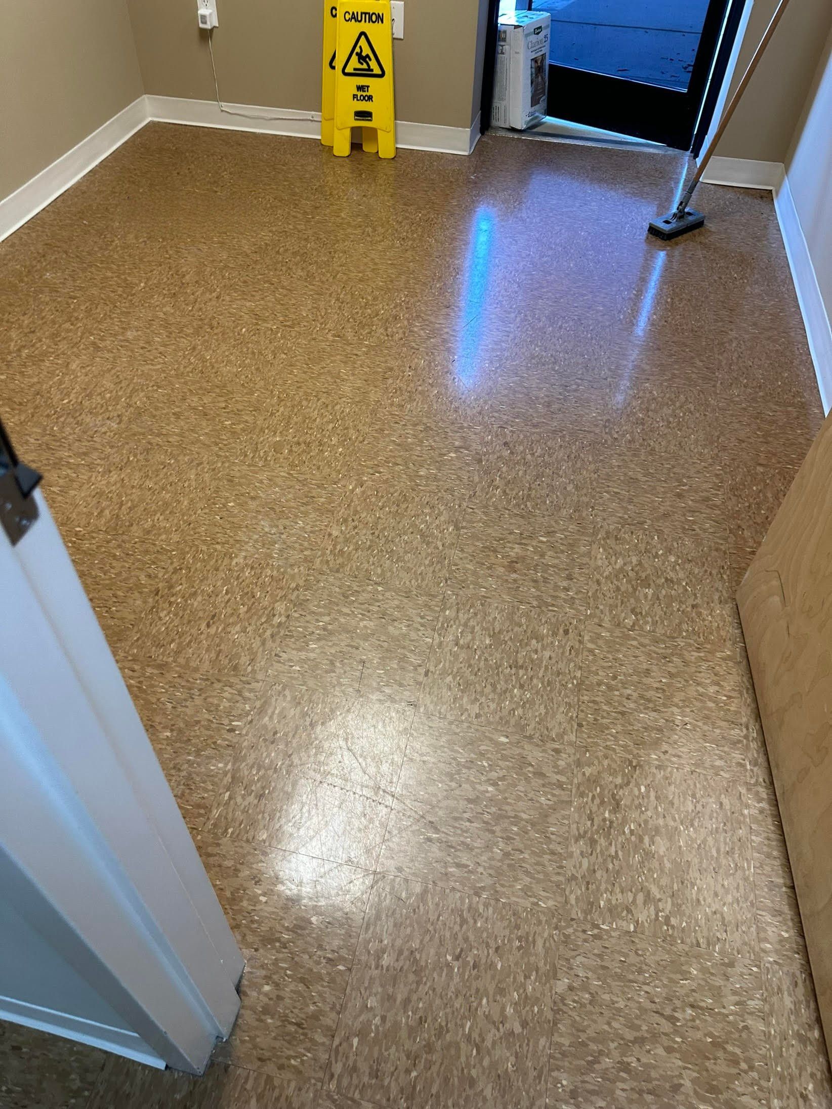 Brown speckled floor with a caution sign, doorway, and cleaning supplies.