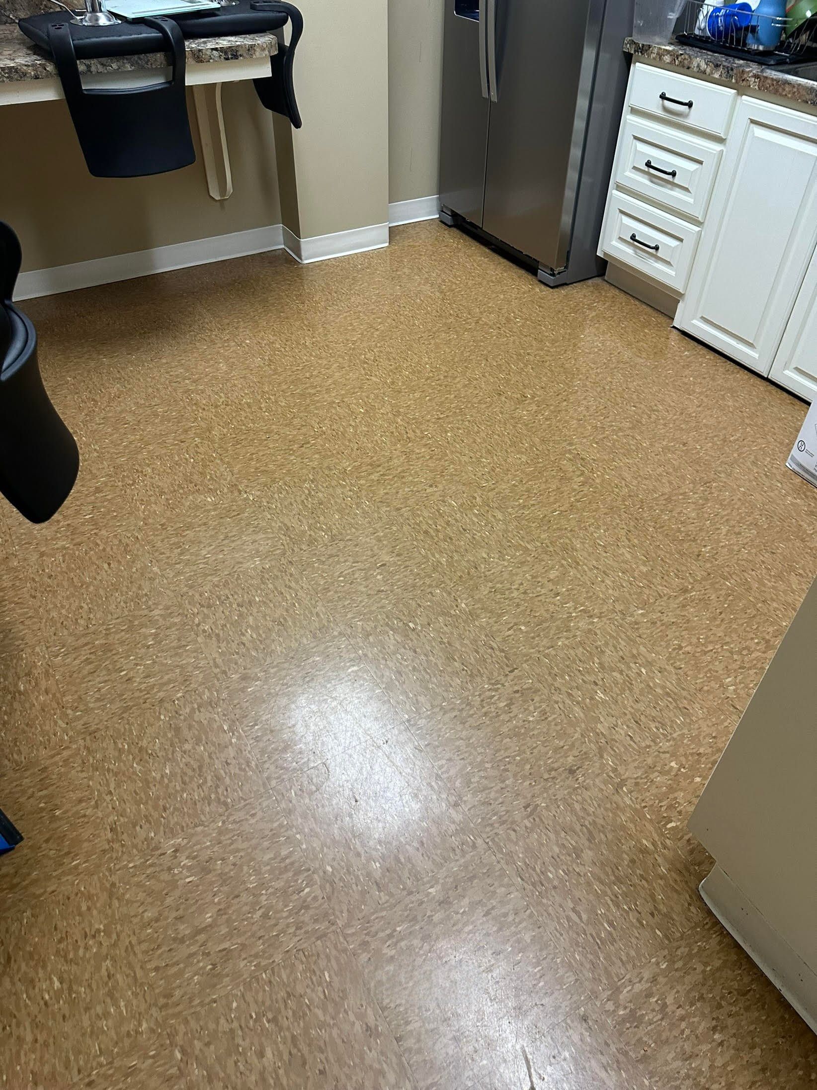 Cork flooring in a kitchen with white cabinets and a stainless steel refrigerator.
