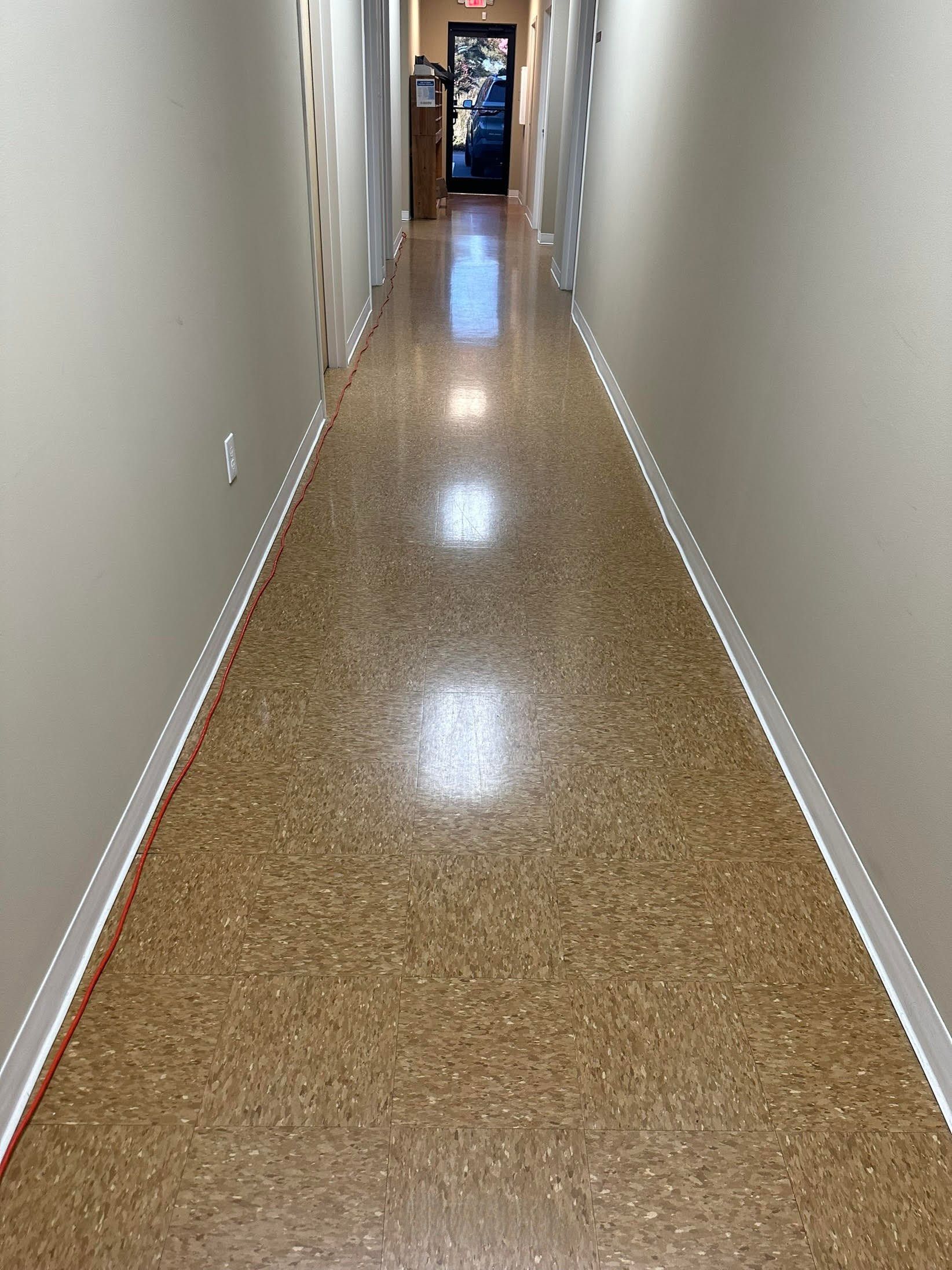 Narrow hallway with cork flooring and beige walls, leading to a door at the end.