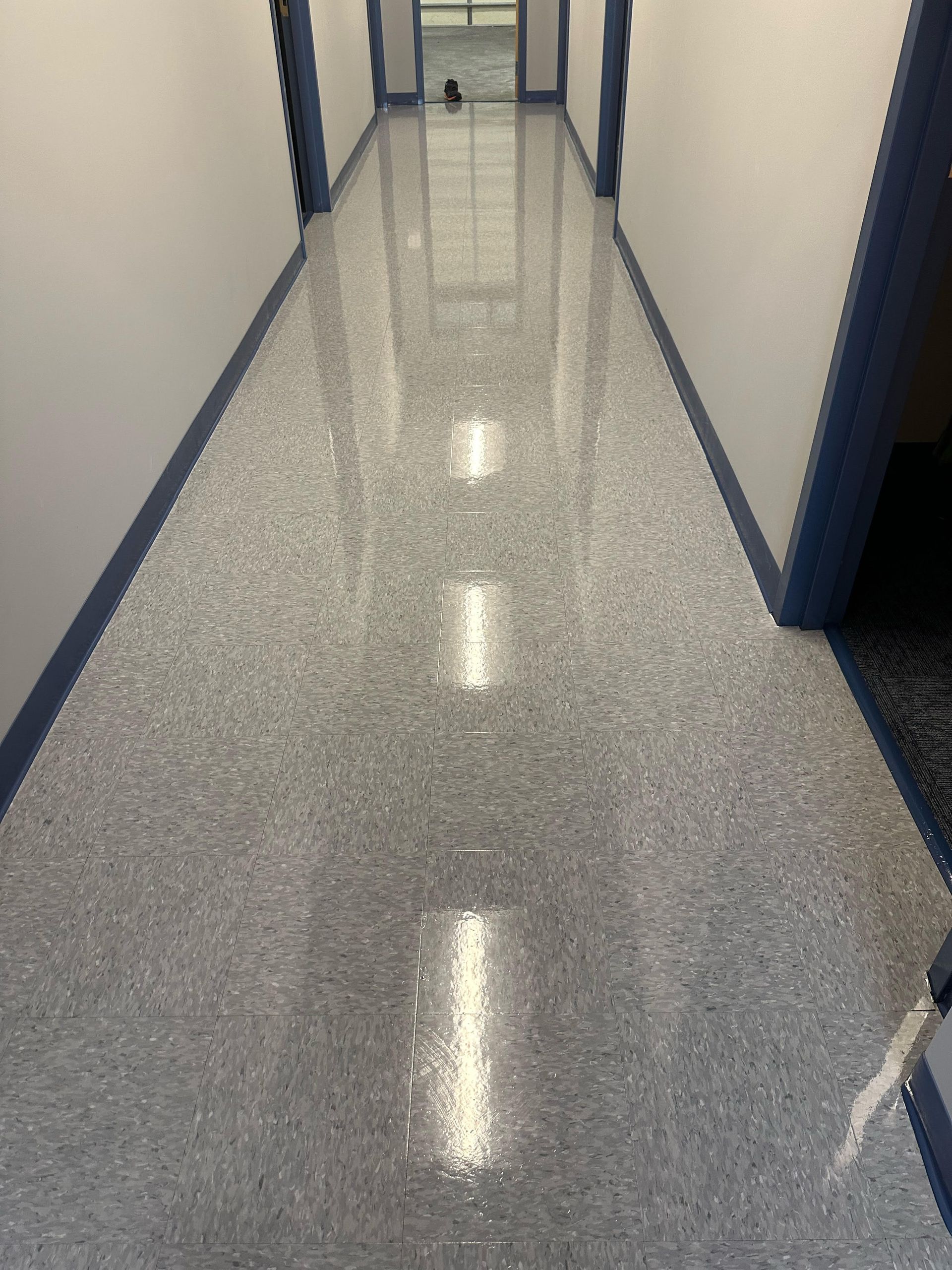 Long, narrow hallway with speckled gray flooring, white walls, and blue trim.