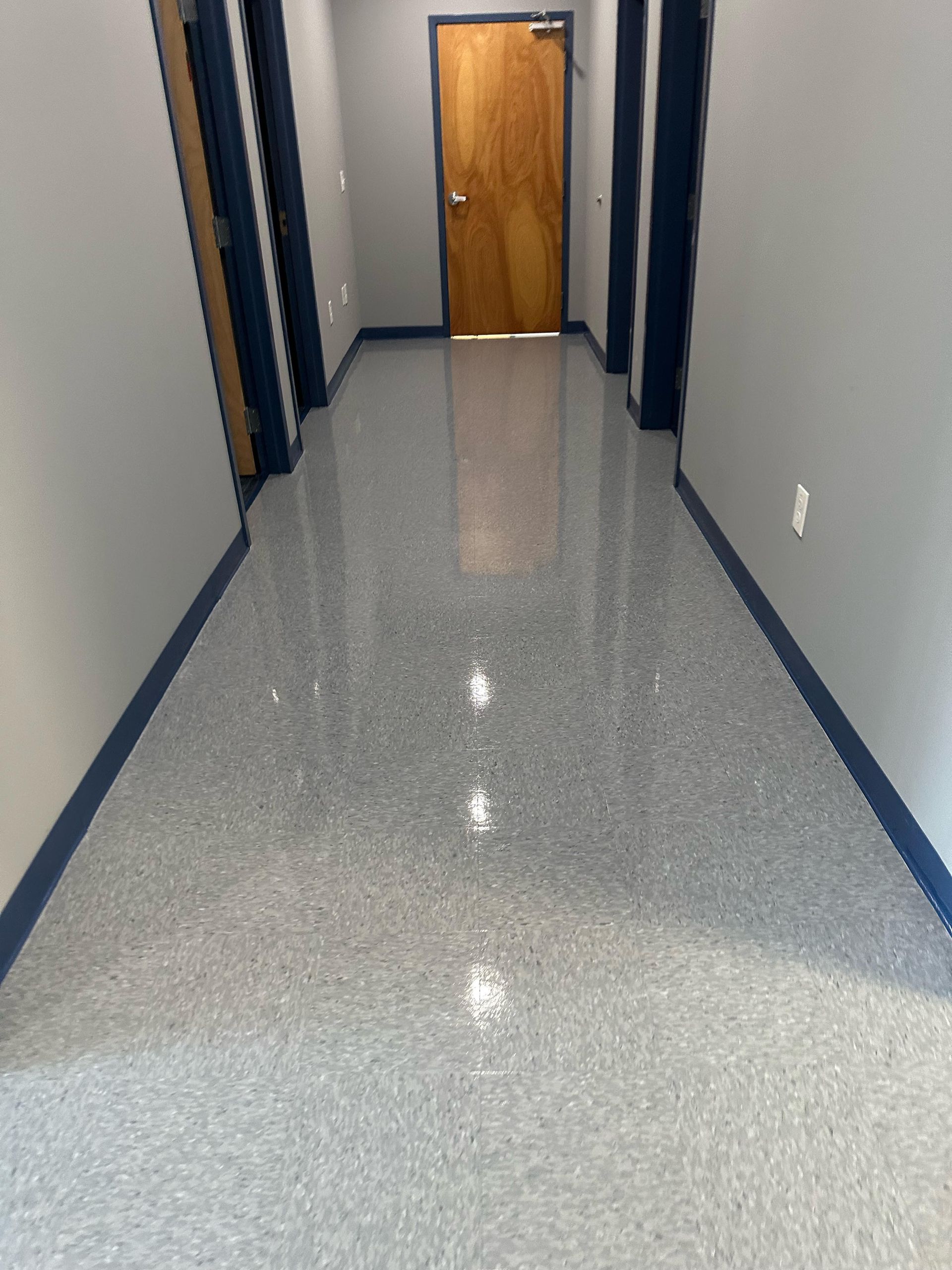 Long hallway with glossy gray speckled floor, blue trim, and a wooden door at the end.