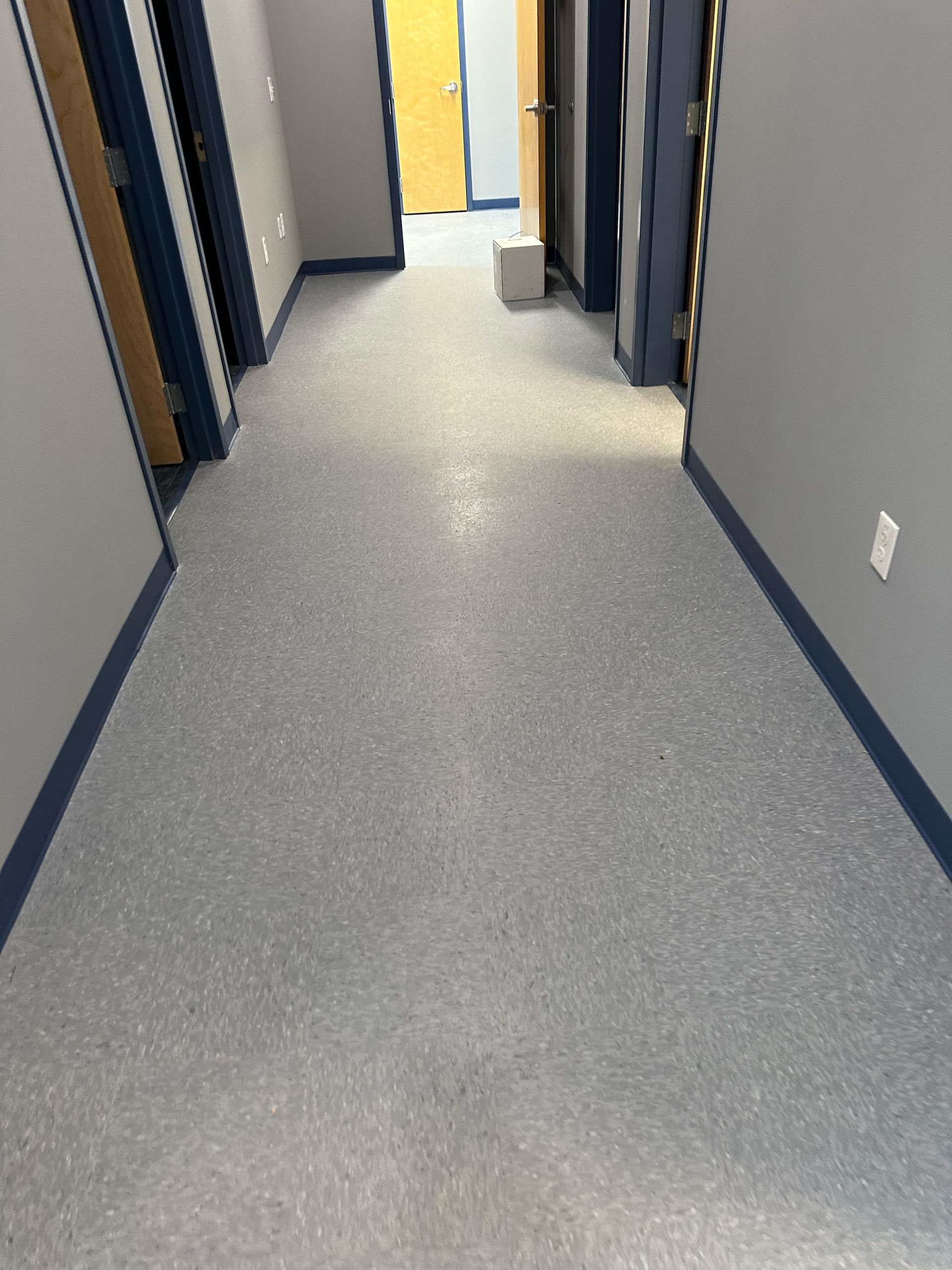 Long hallway with gray speckled flooring and gray walls. Blue trim around doors and baseboards.