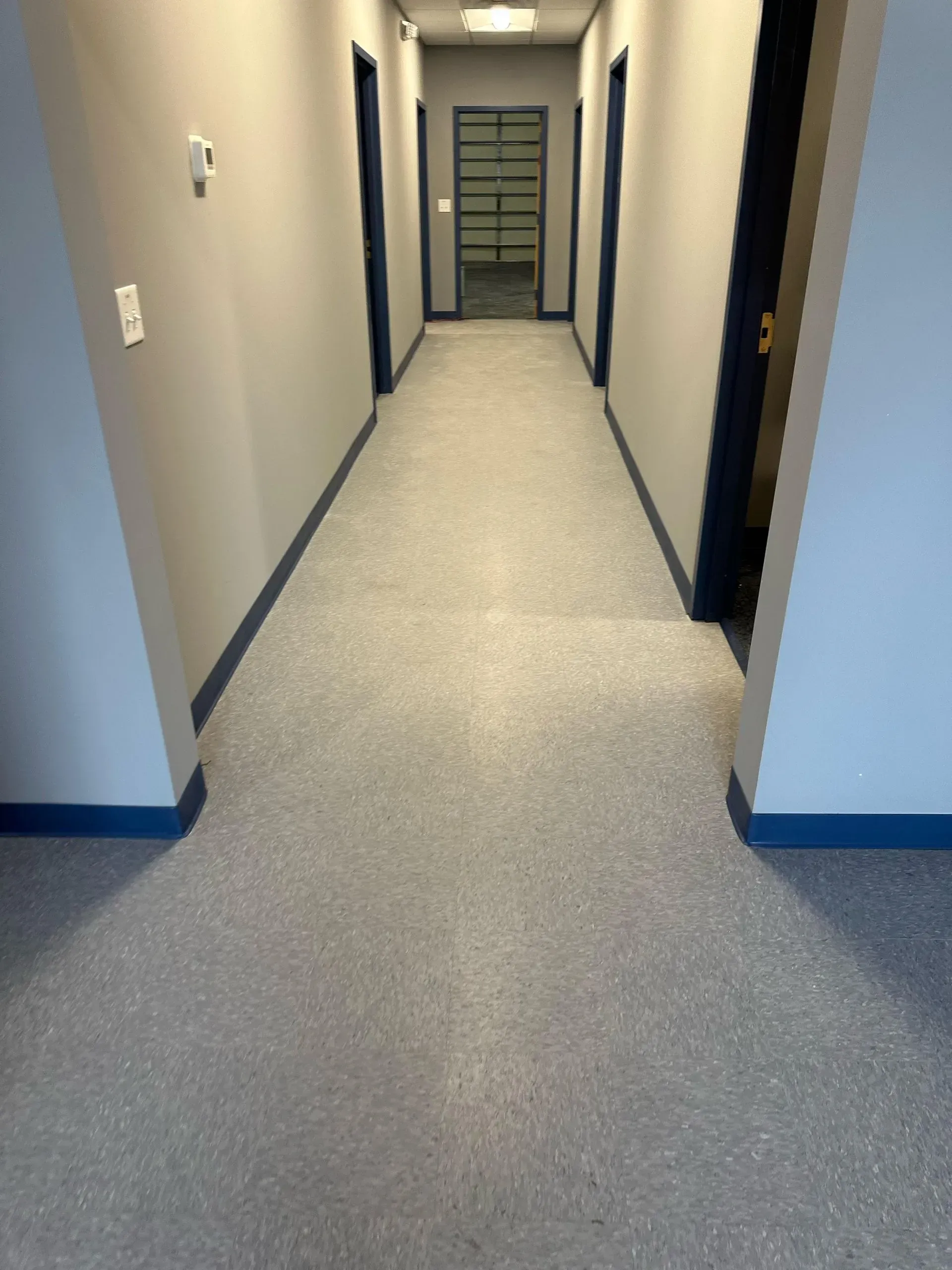 Hallway with gray speckled floor, blue baseboards and door trim, and gray walls.