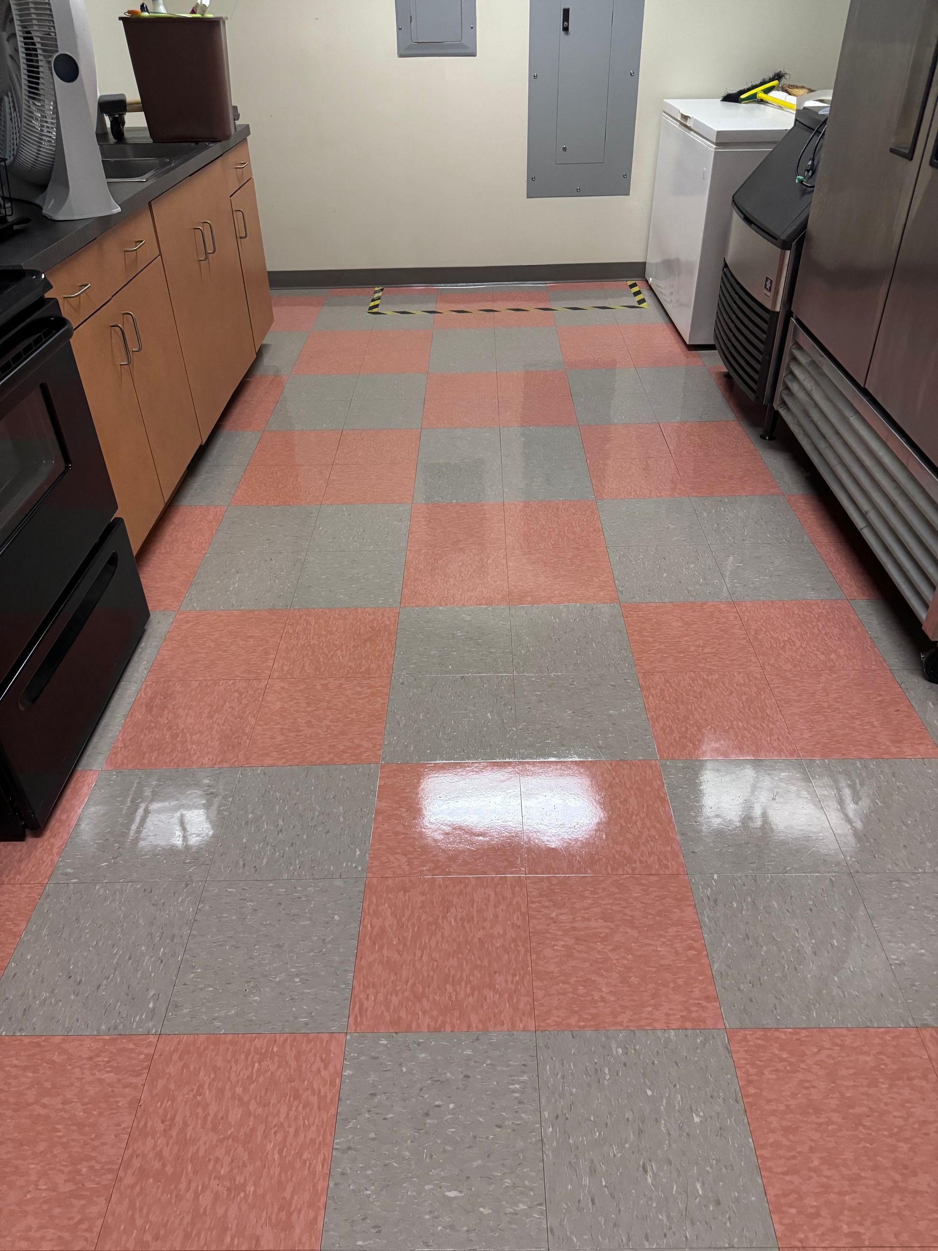 Red and gray checkered tile floor in a commercial kitchen with appliances and cabinets.