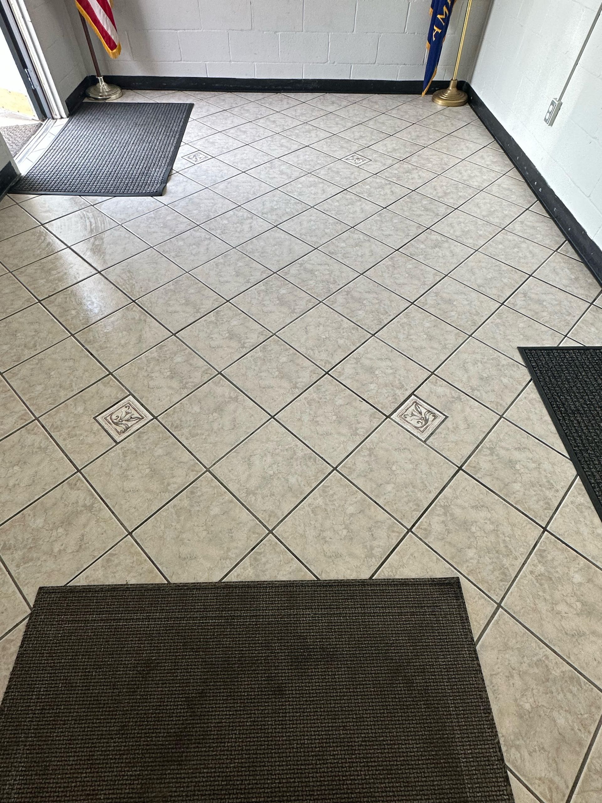 Entryway with gray mats, light tile floor in a diagonal pattern, flags, and black trim.