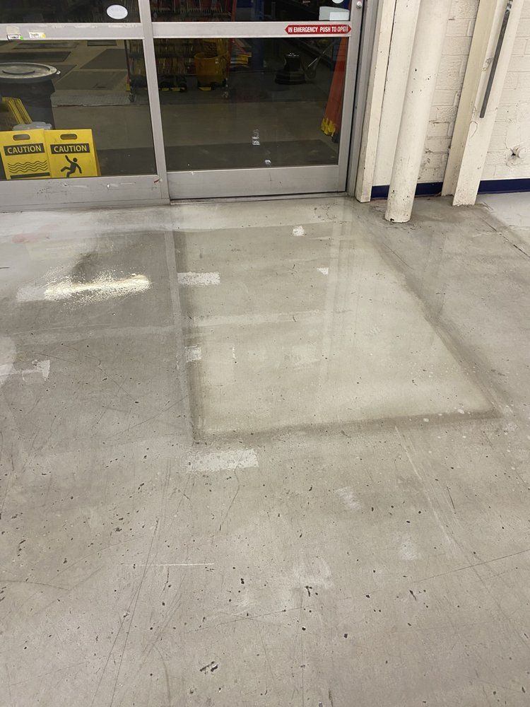 Wet concrete floor inside a store near entrance doors. A caution sign is visible.