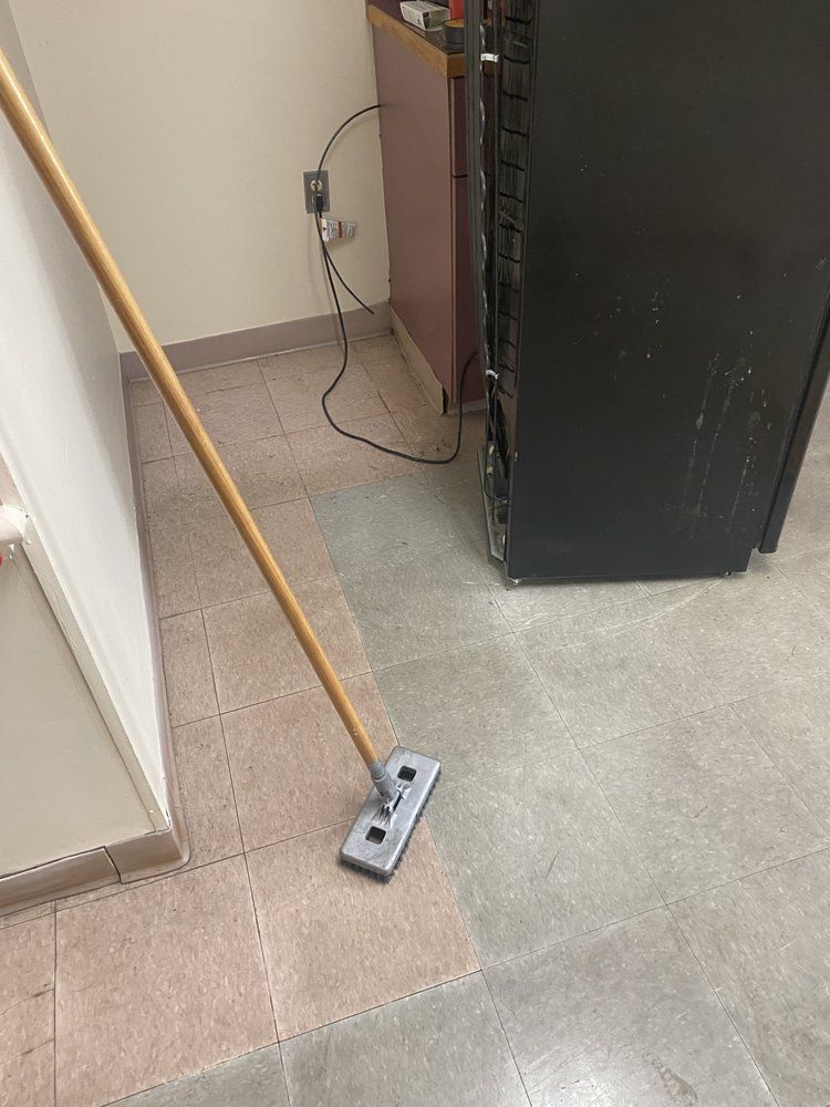 A mop on a floor cleaning an area, next to a black cabinet and tan wall.