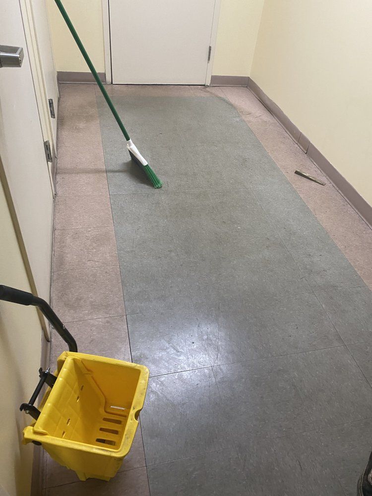 A hallway with a green-gray floor, yellow mop bucket, and a mop leaning against the wall.