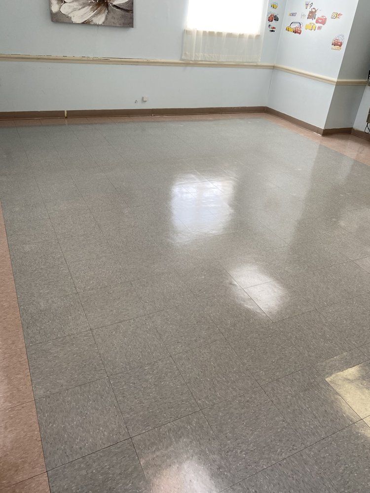 Empty room with shiny, gray tiled floor. Pale walls, border trim, and a window with sheer curtains.