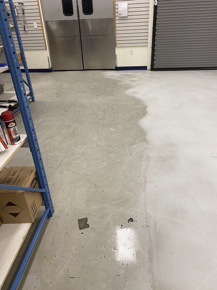 Warehouse floor, part cleaned, with a clear line of demarcation. Shelving and double doors in background.