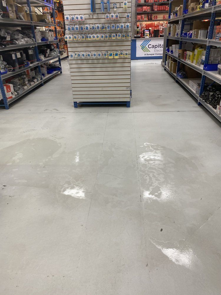 Water spots on a light gray industrial floor in an aisle of a store, surrounded by shelving with products.