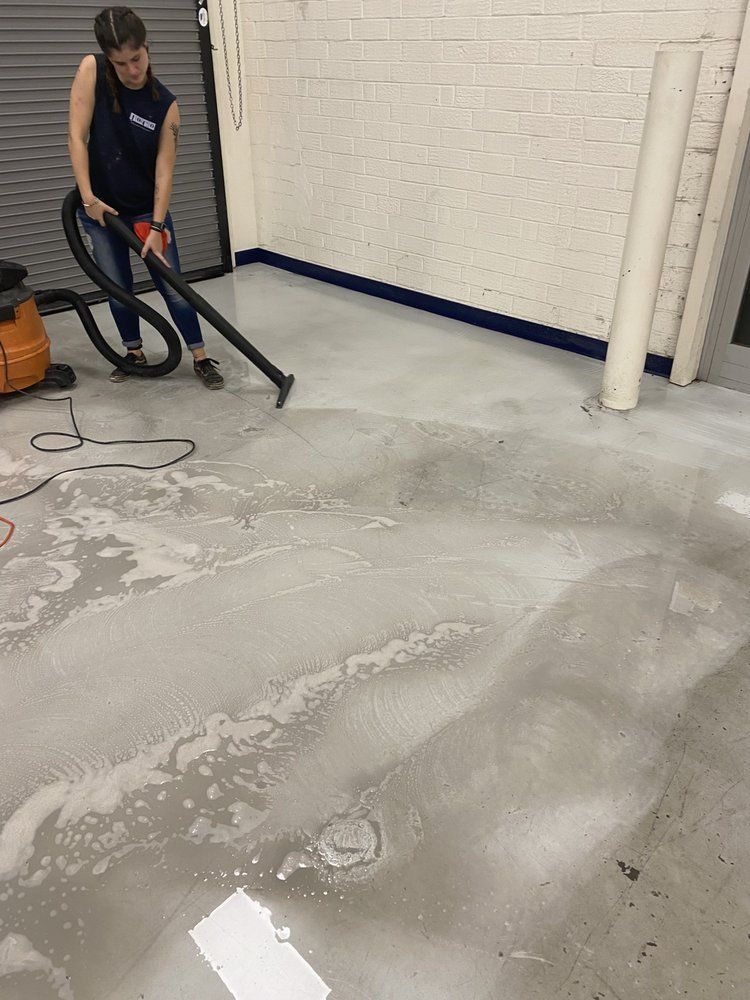 Person vacuuming a wet, gray floor with suds, in a room with white brick wall.