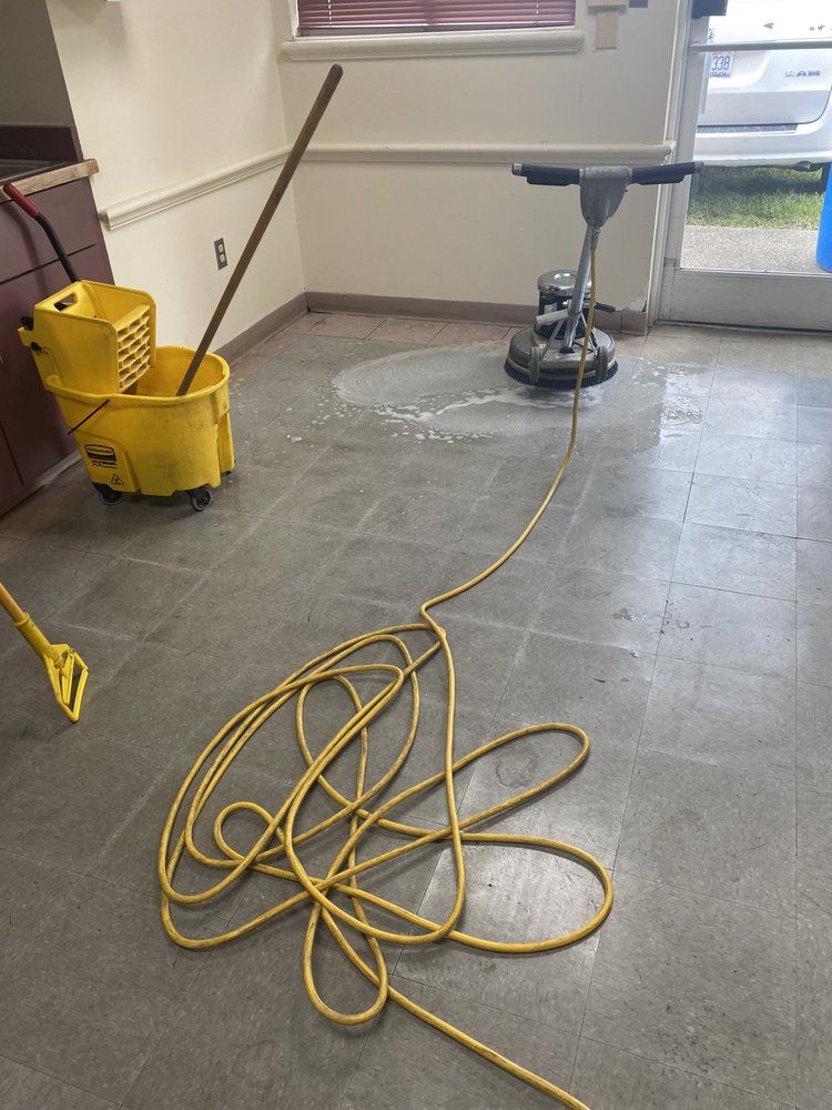 Cleaning a concrete floor with a floor buffer, mop bucket, and coiled yellow extension cord.