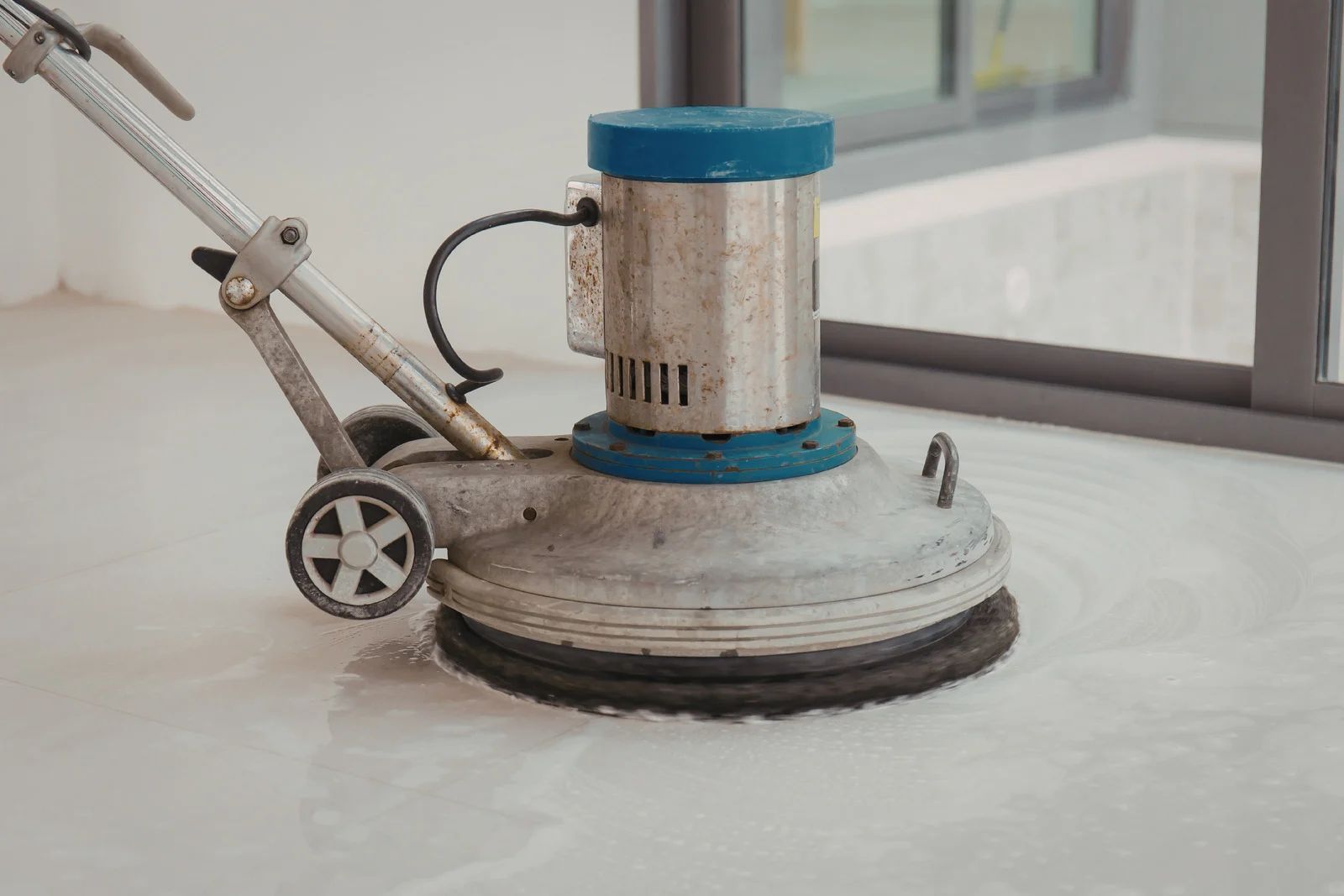 Floor buffer machine with a blue top cleaning a glossy white floor