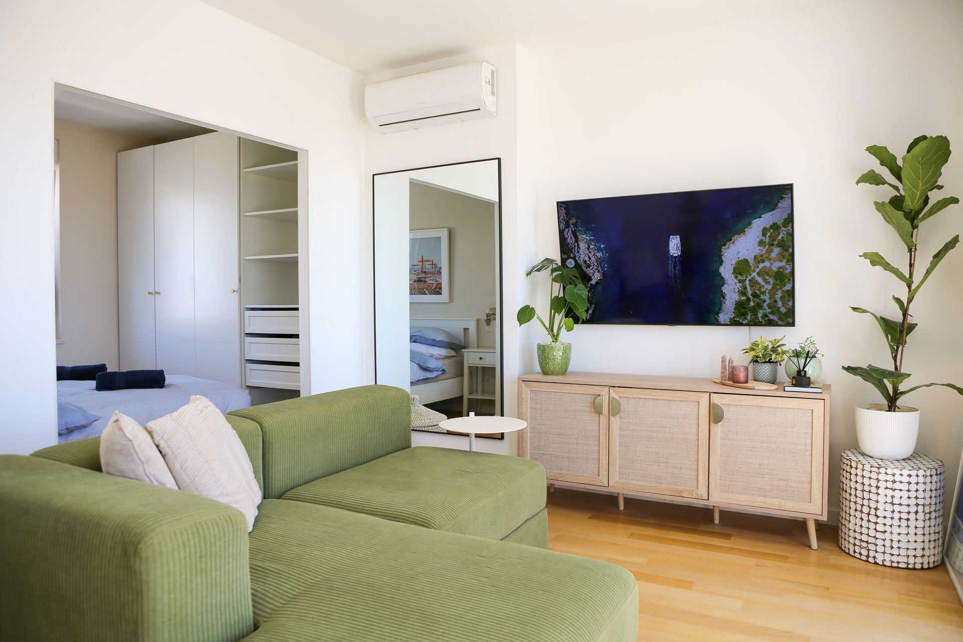 Green sectional sofa in a bright living room, with a TV, mirror, and closet visible.