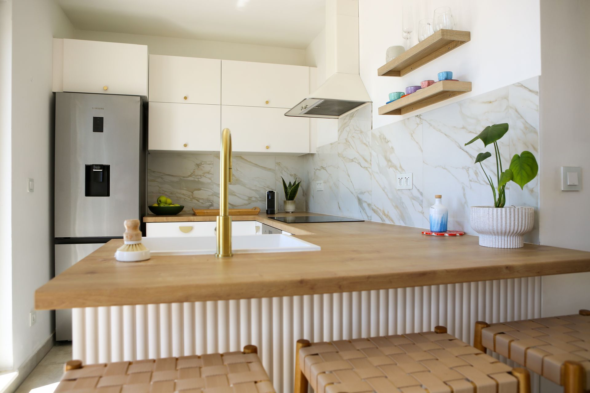 Modern kitchen with white cabinets, wood countertop, gold faucet, and seating.